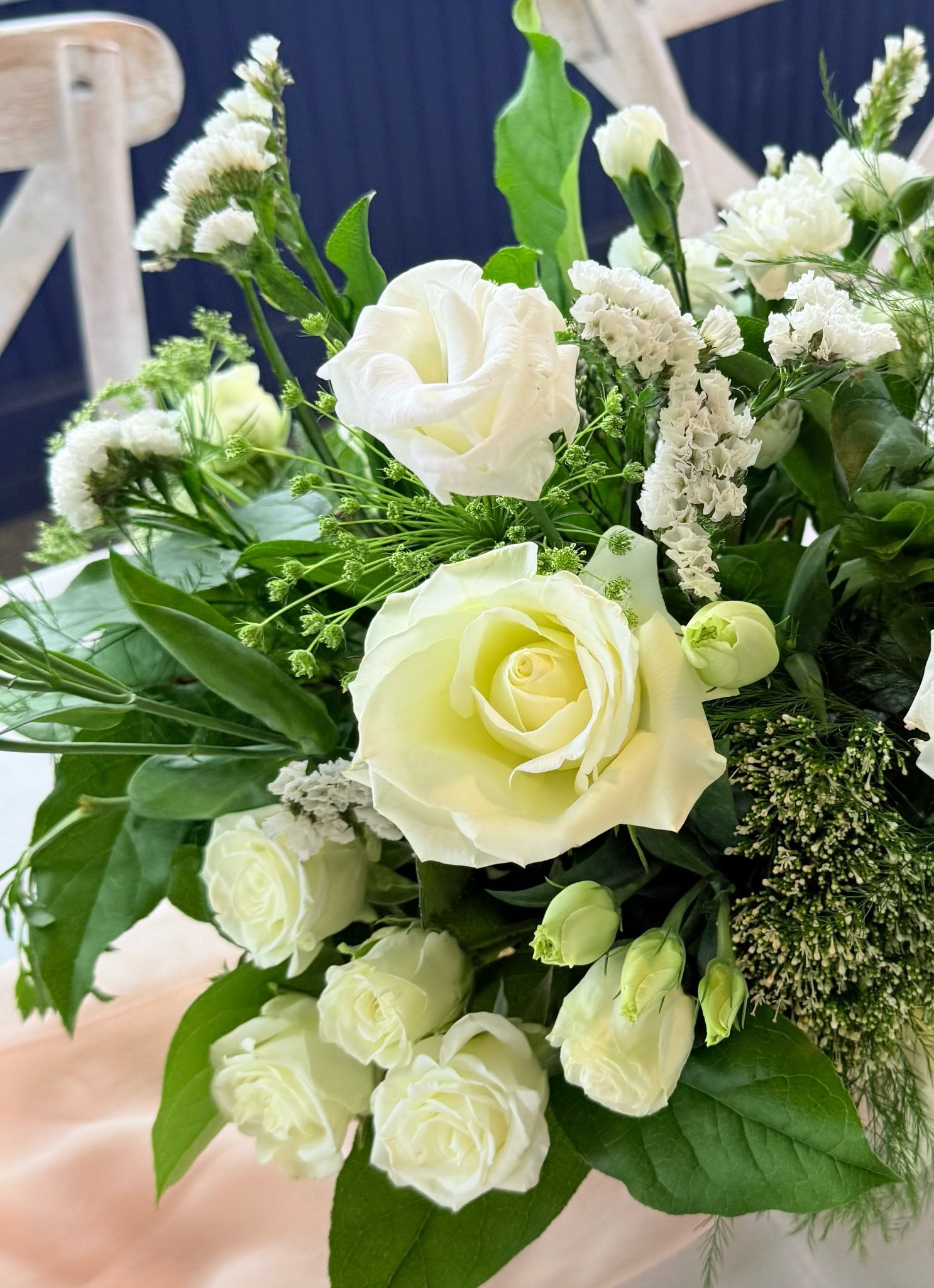 A bouquet of white roses, lisianthus, and other white flowers with green leaves.