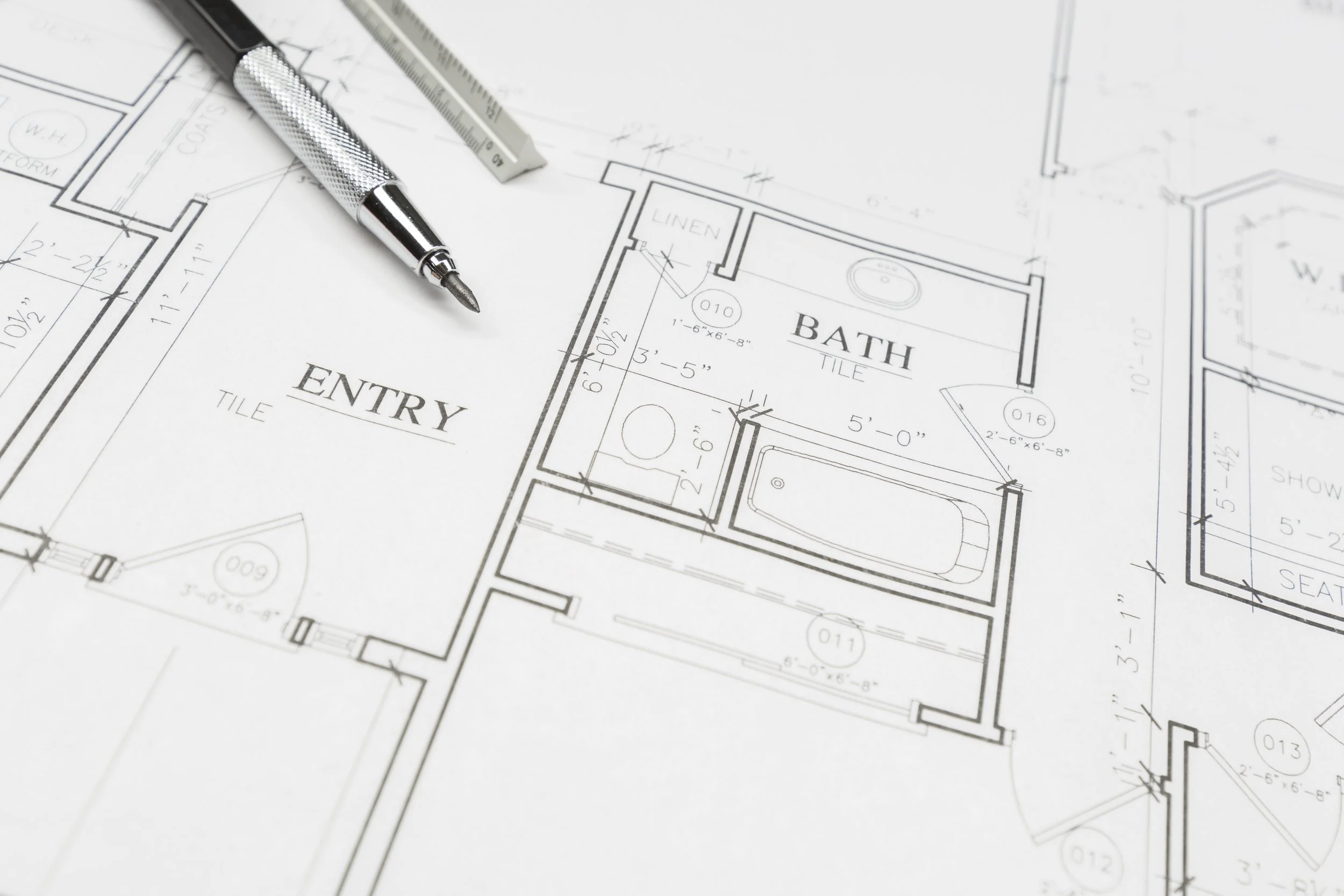 Architectural blueprint of a house floor plan with labeled rooms such as ENTRY and BATH, with a silver pen and ceramic knife placed on top of it.