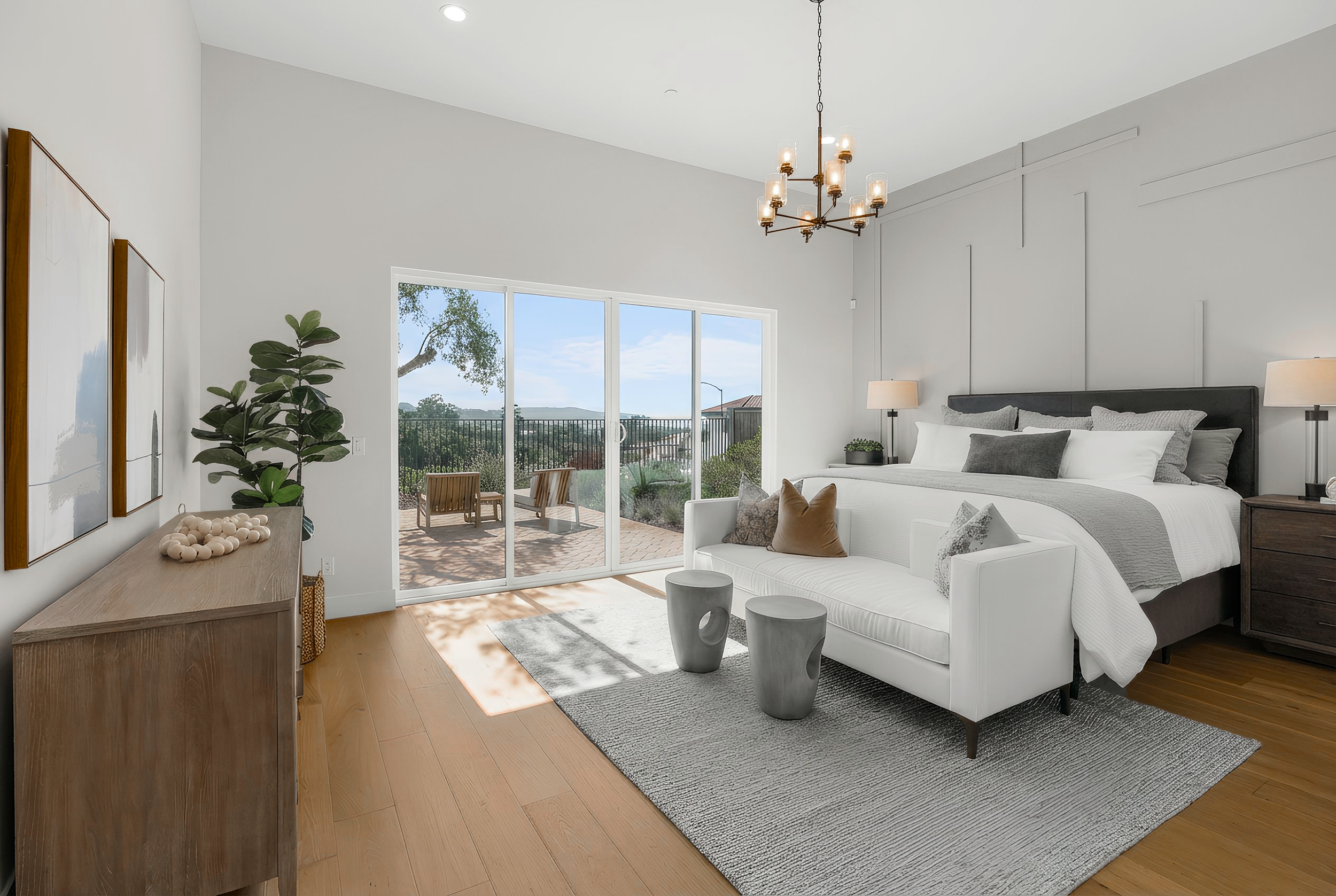 Modern bedroom with sliding glass door leading to a balcony, white sofa, bed with gray bedding, wooden floor, and minimal decor.