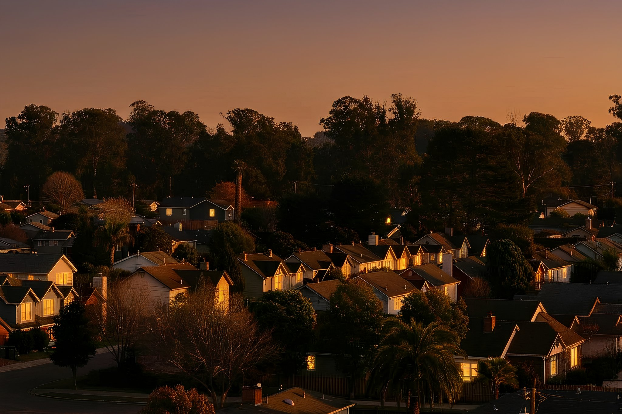 Residential neighborhood at sunset with houses, trees, and a colorful sky.