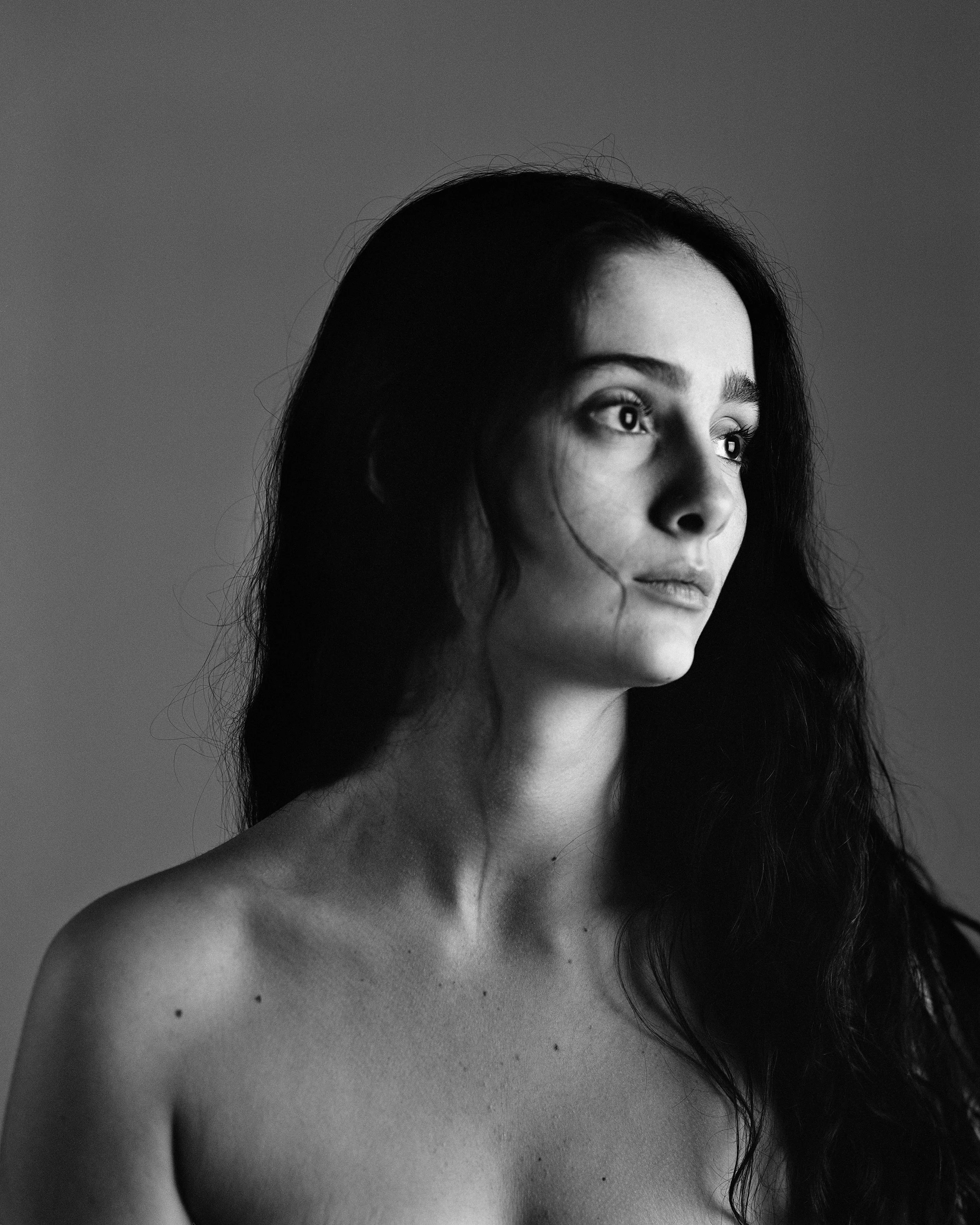Black and white portrait of a young woman with long dark hair, looking thoughtful, with a neutral expression. The image emphasizes her face and shoulders against a plain background.