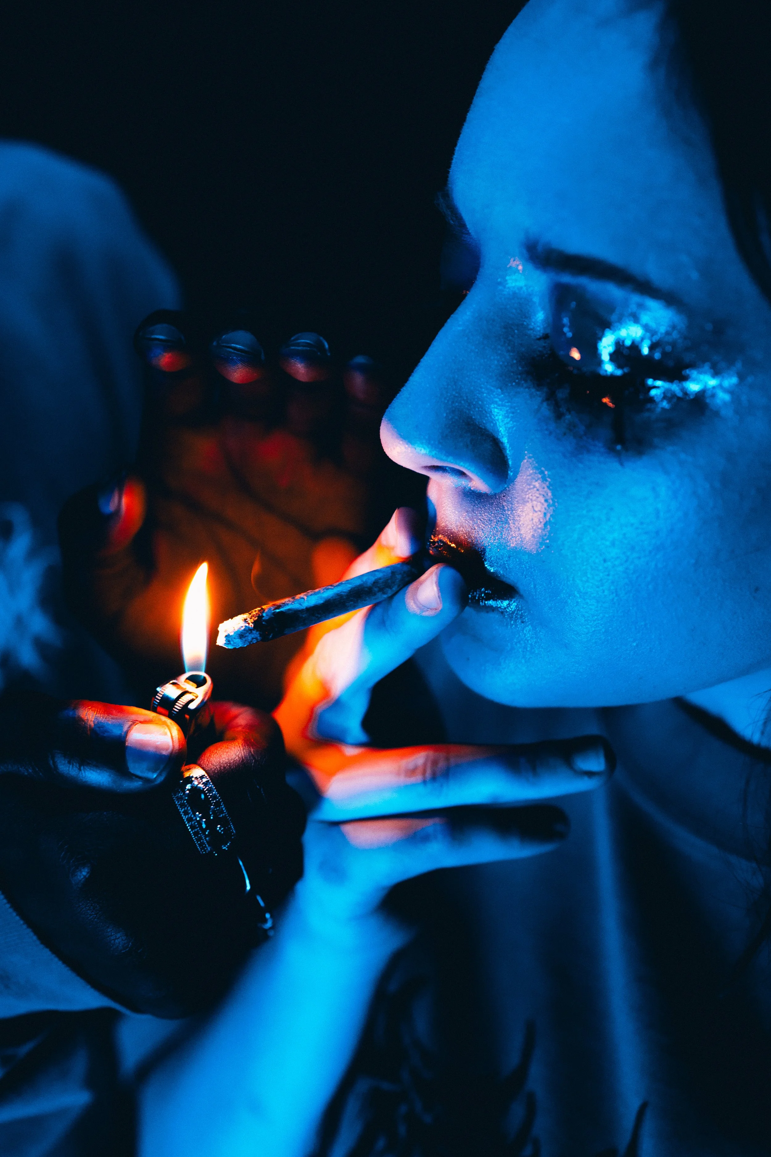 Close-up of a person lighting a Ceremony preroll with a lighter, with blue lighting.