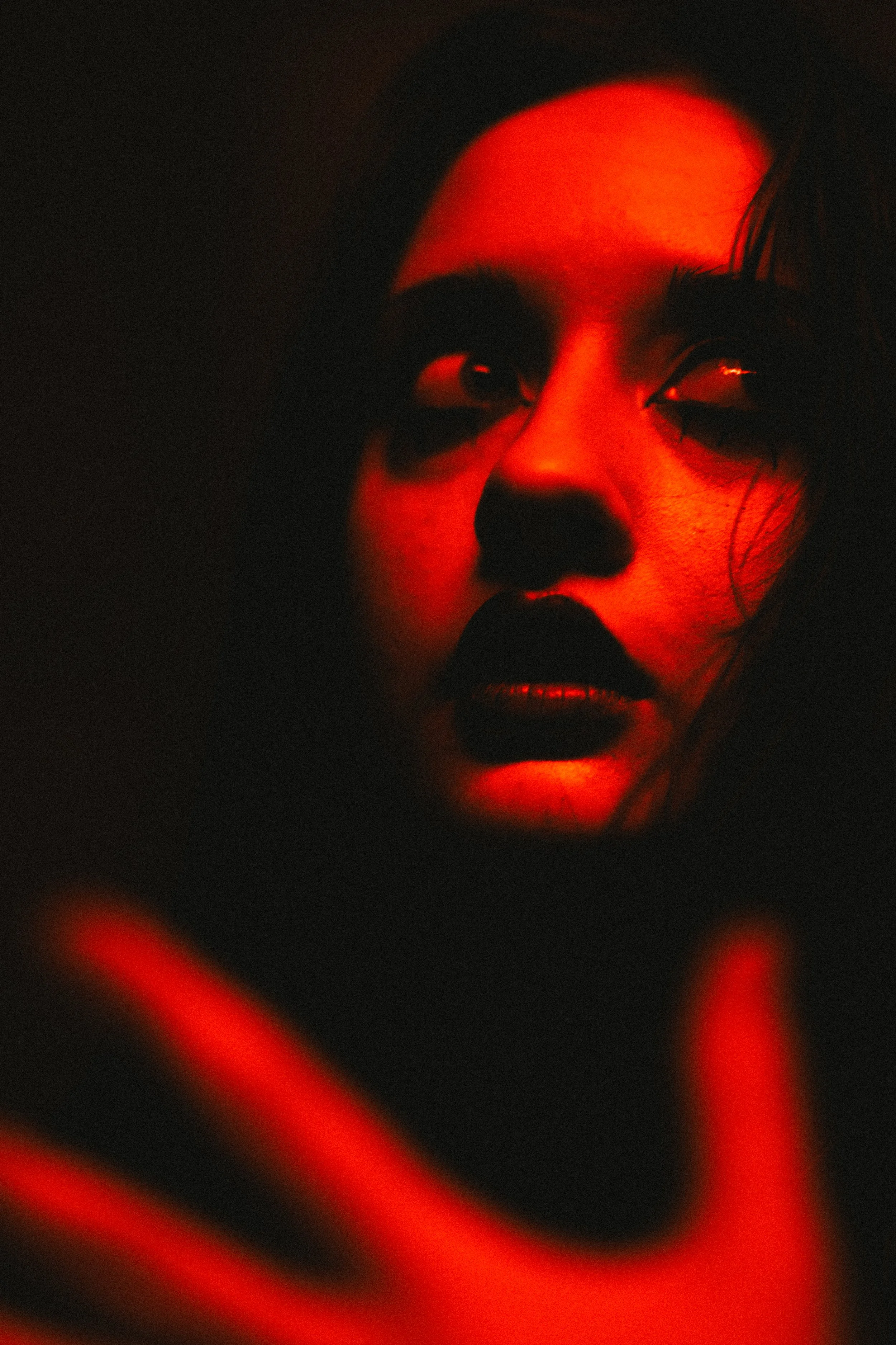 Close-up of a person with dramatic red lighting and shadows, showing a pensive expression.