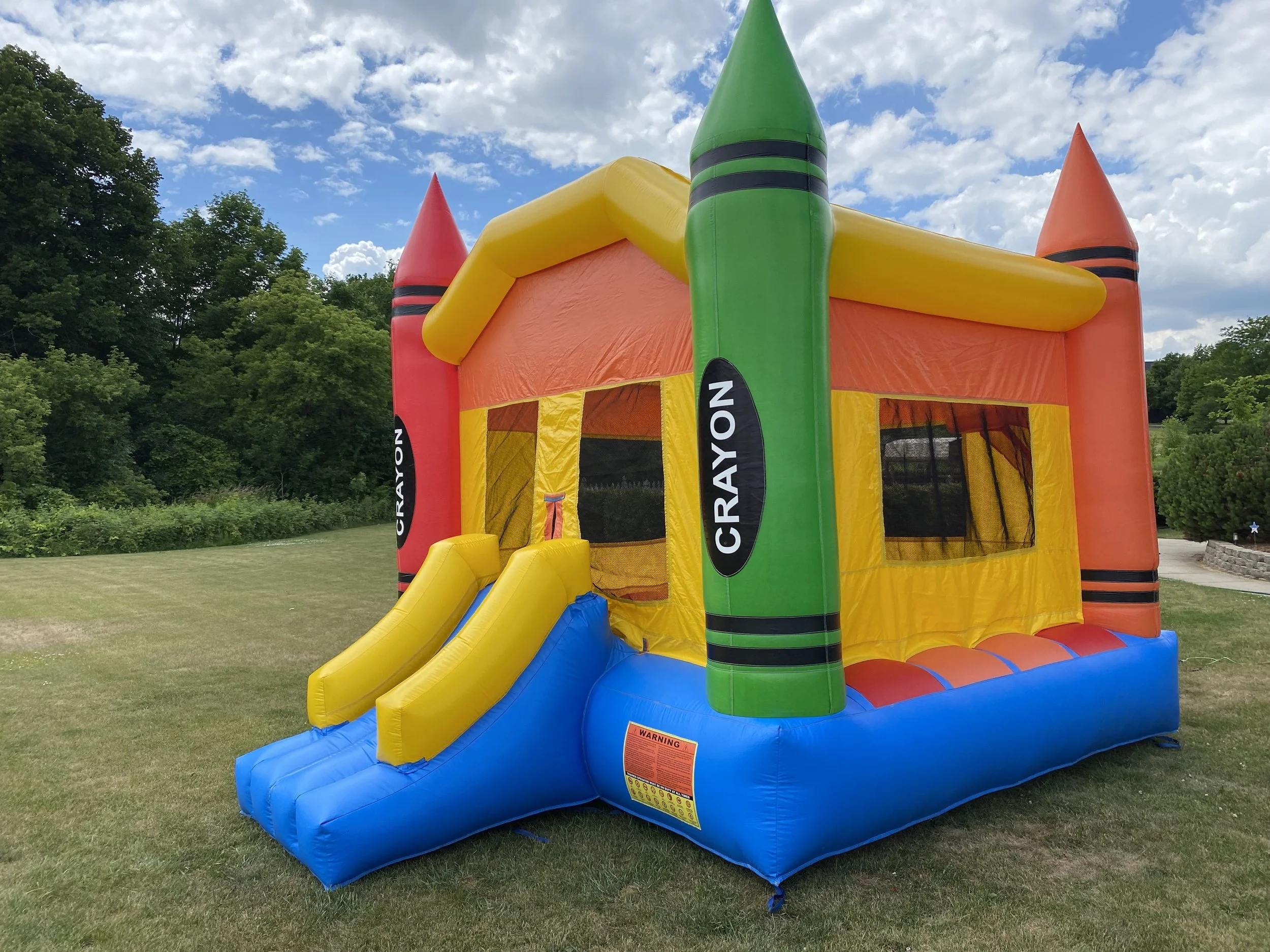 Colorful inflatable bounce house shaped like crayons on a grassy lawn.