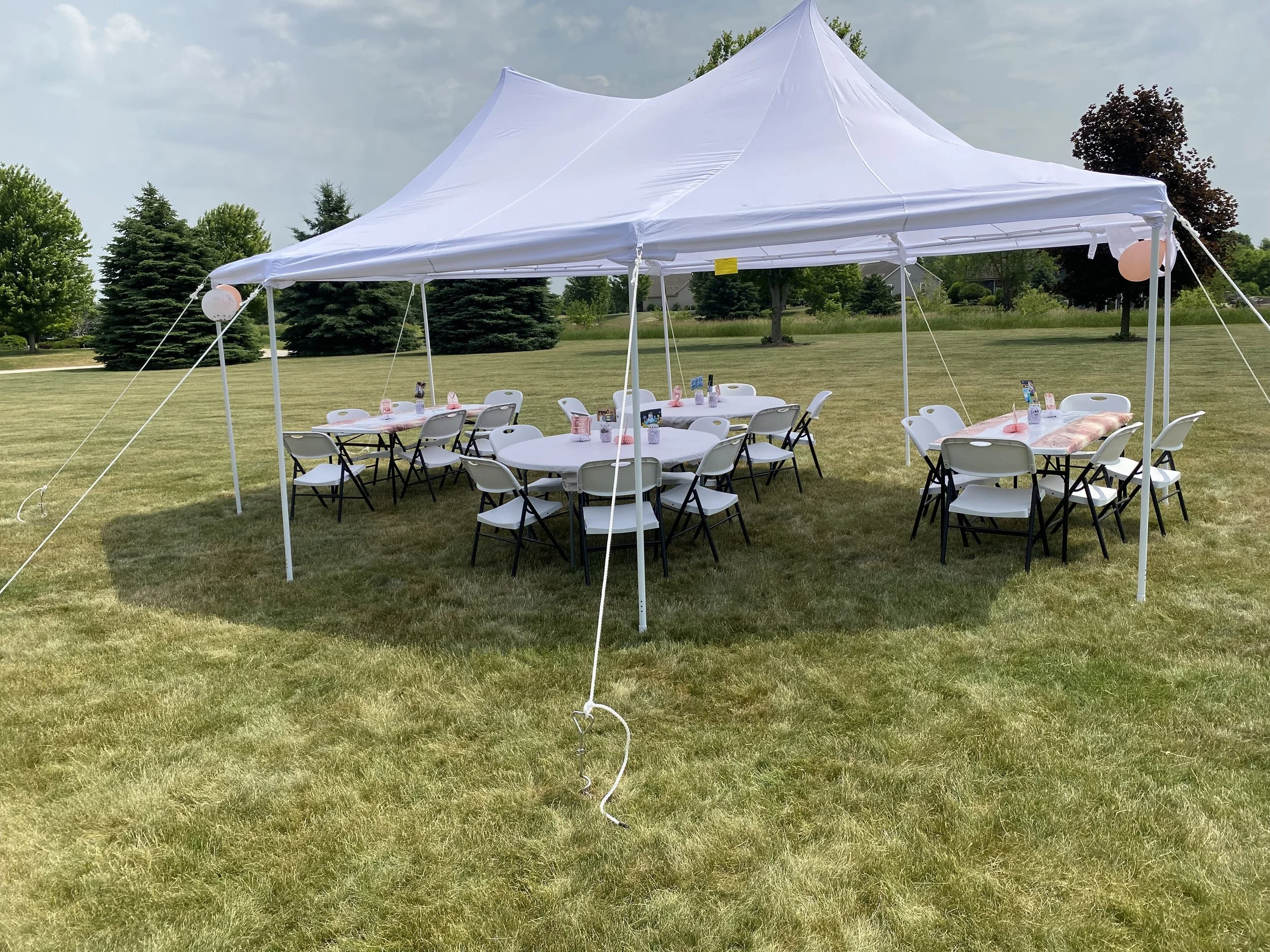 Outdoor tent with tables and chairs set up for an event on a grassy field.