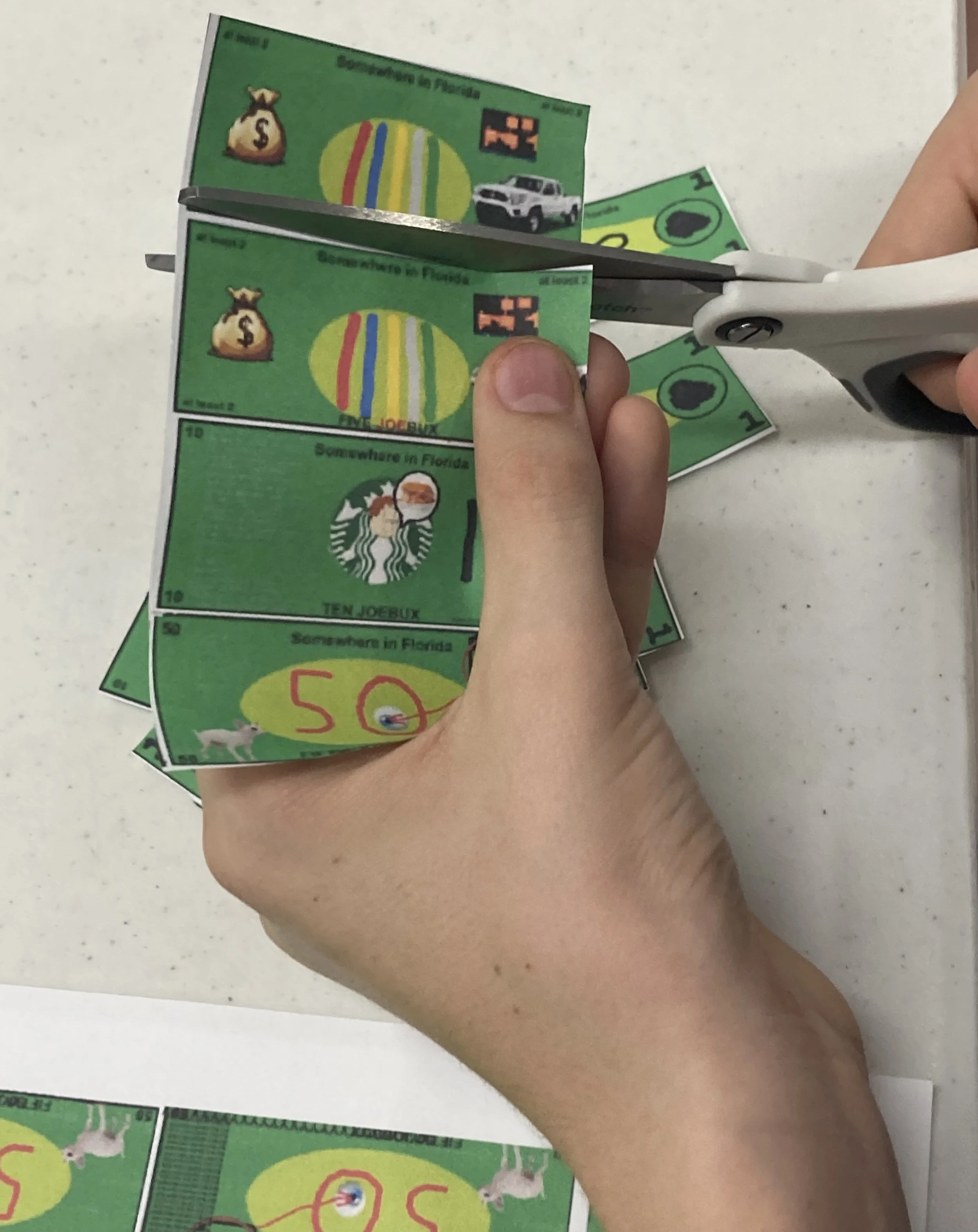 Person cutting printed play money labeled "Somewhere in Florida" with scissors
