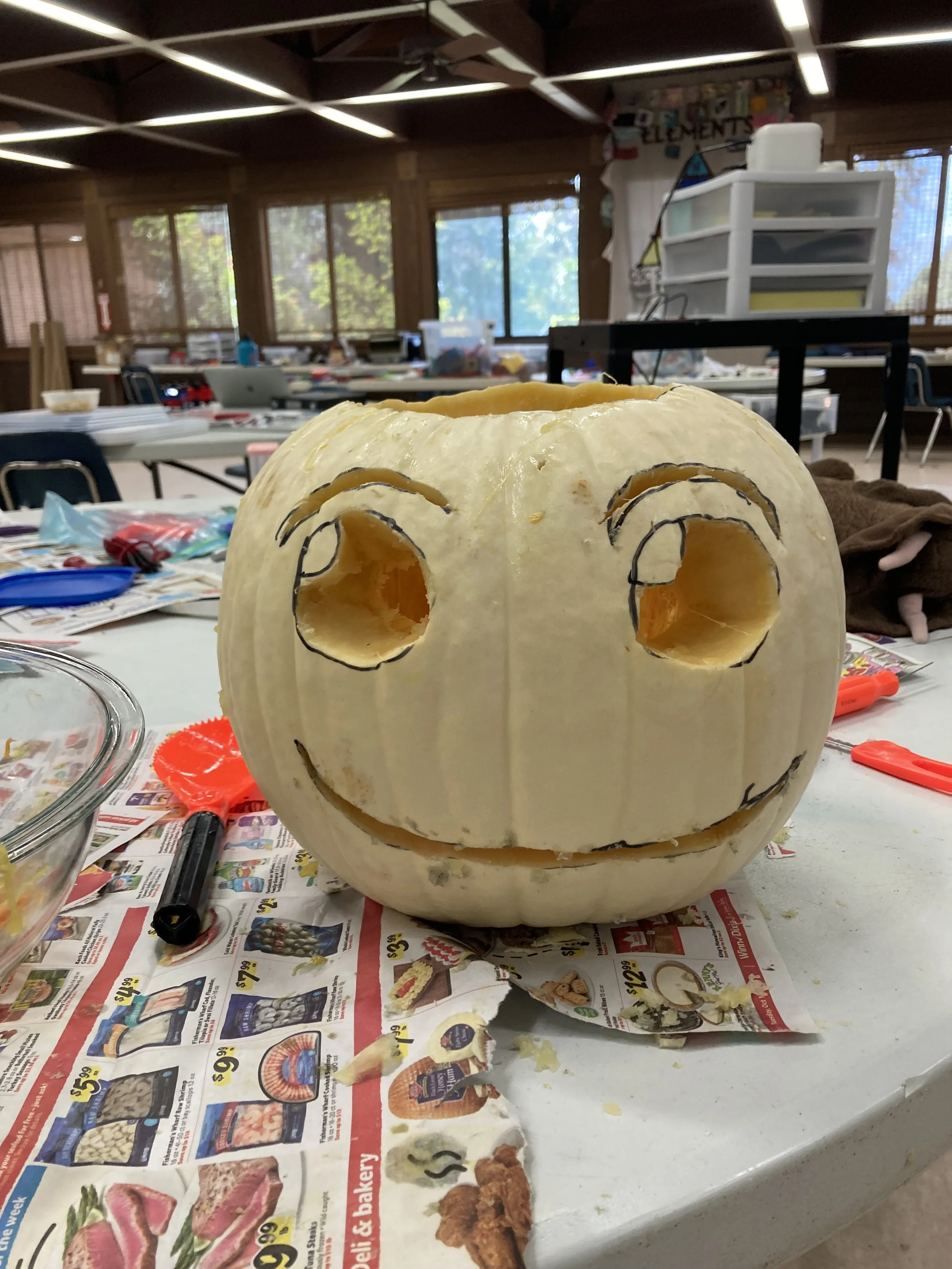 Carved white pumpkin with face design on a table in a workshop setting.