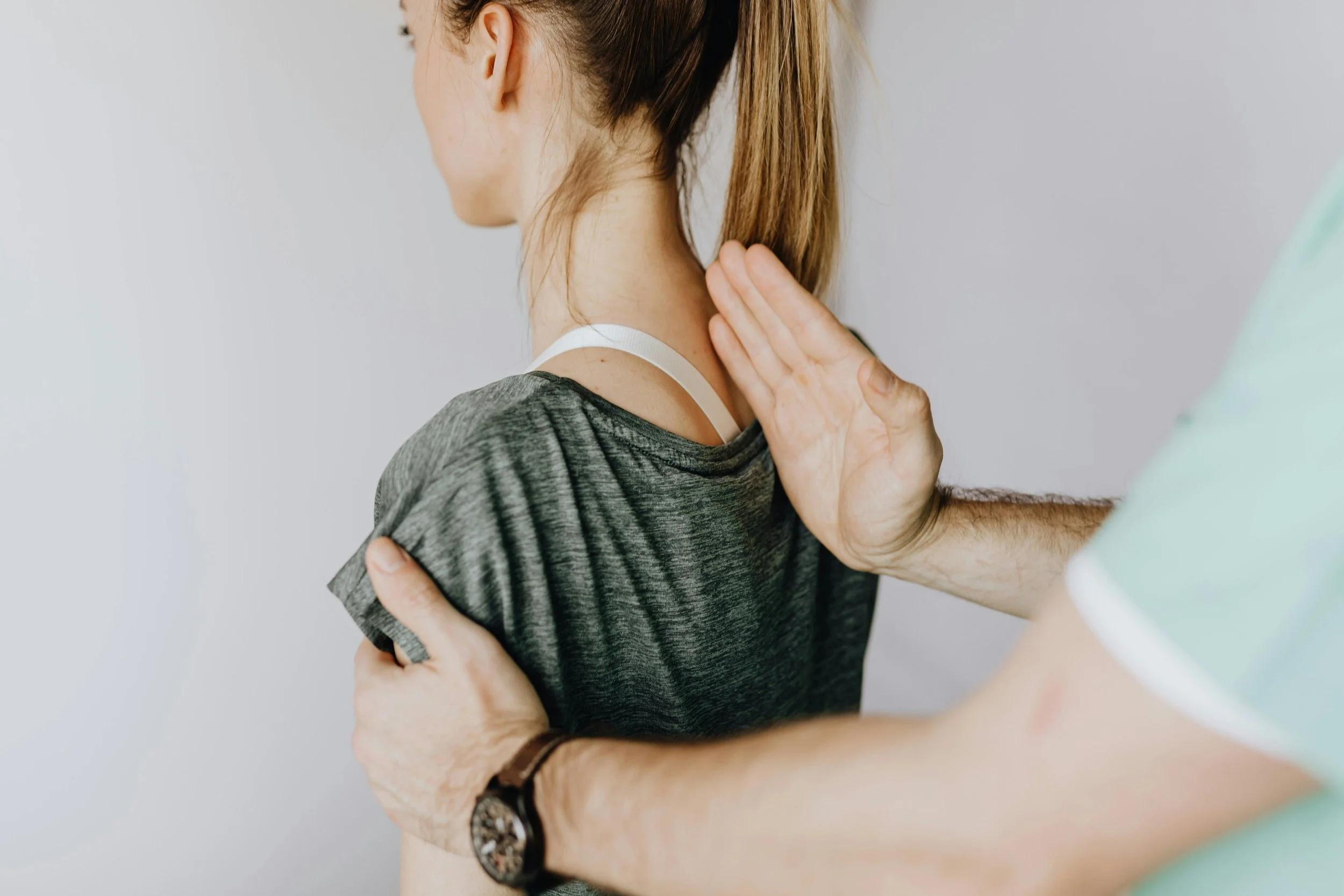 Someone evaluates a woman's upper spine and neck alignment by positioning her shoulders and assessing her posture. Reflecting the perspective of Ramneek Bhogal on the role of upper cervical chiropractic in nervous system.
