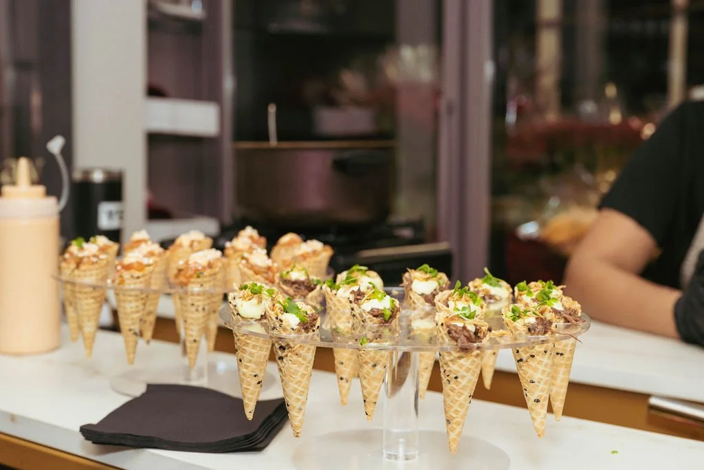 Display of ice cream cones with various toppings on a clear stand in a shop or kitchen setting.