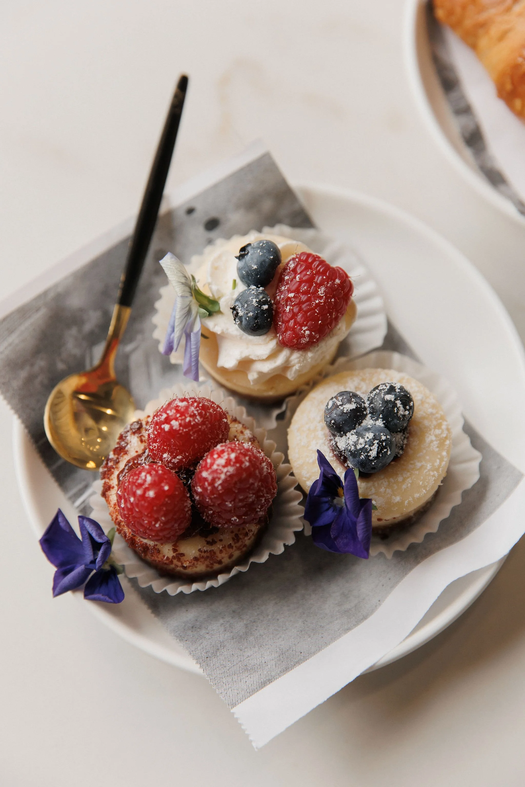 Three small decorated desserts topped with fresh berries and edible flowers on a white plate