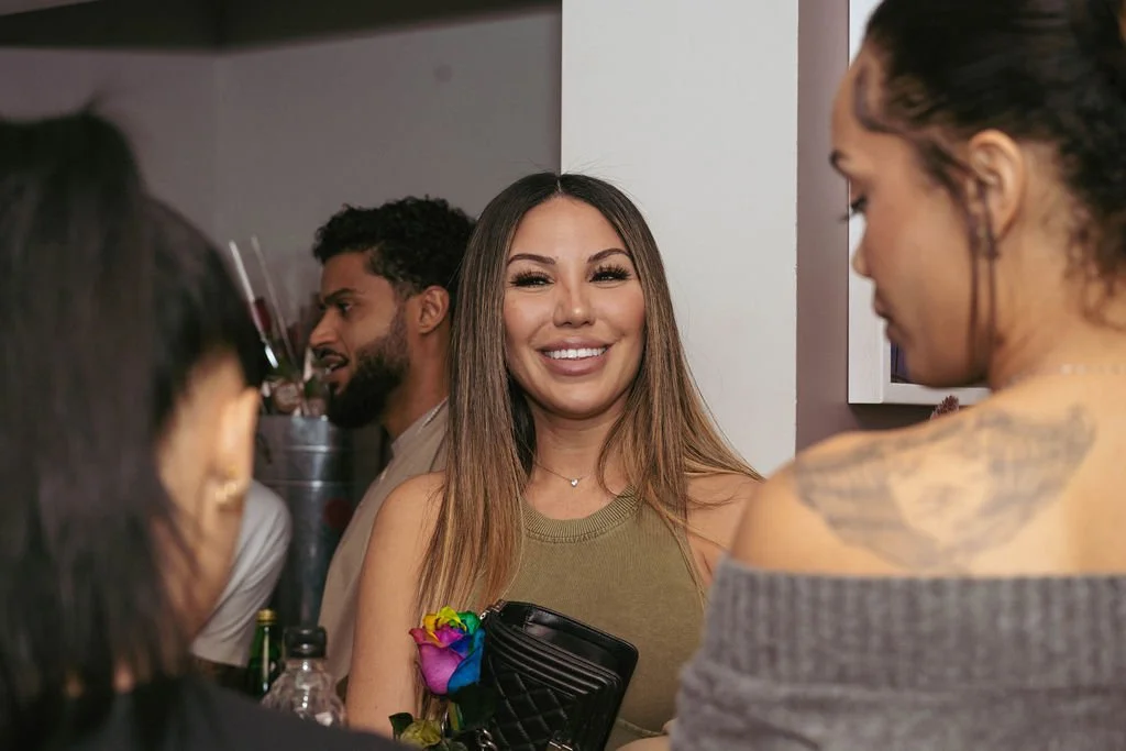 A group of diverse young adults socializing at a party, smiling and talking to each other indoors.