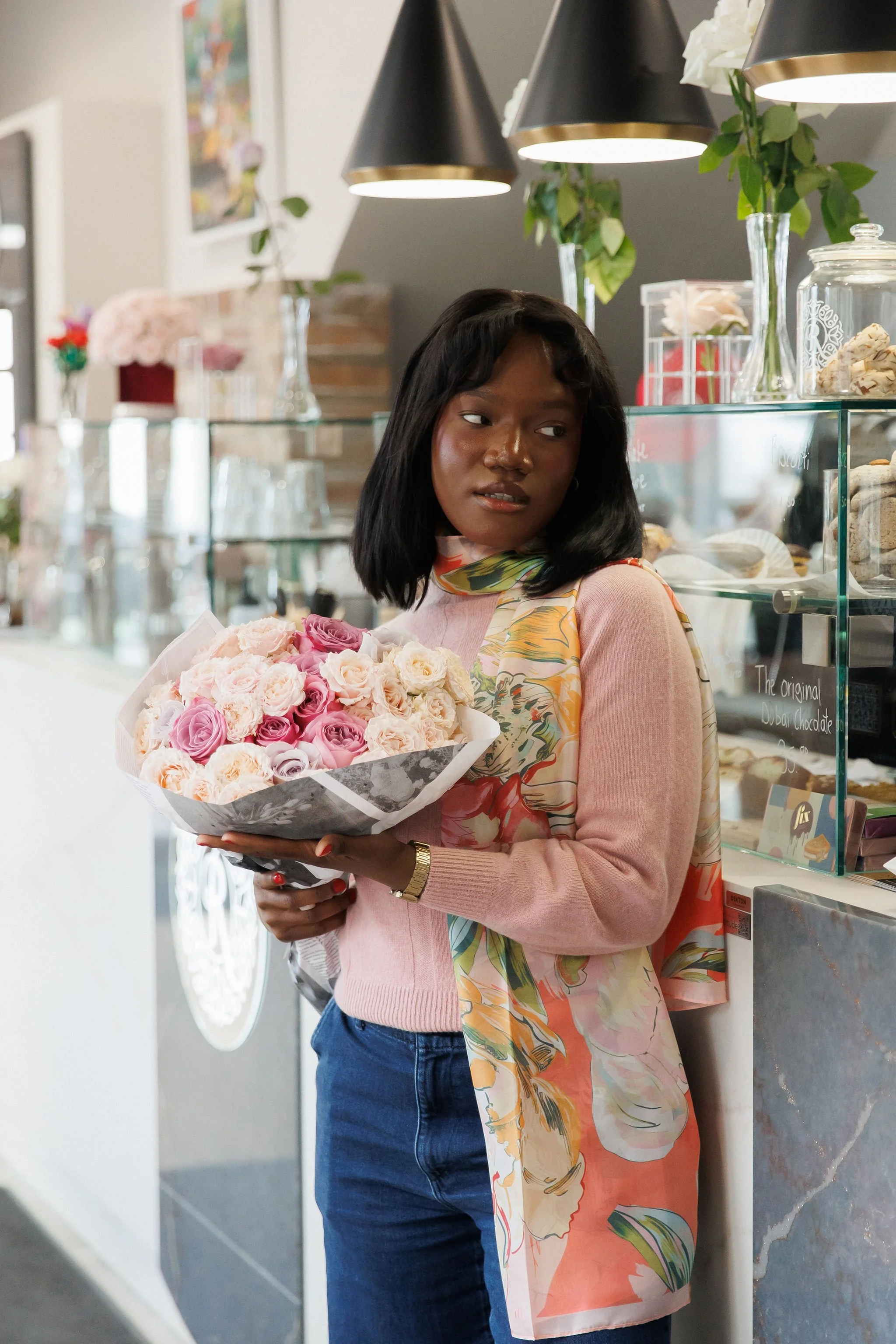 A woman holding a bouquet of pink and white roses inside a bakery or cafe.