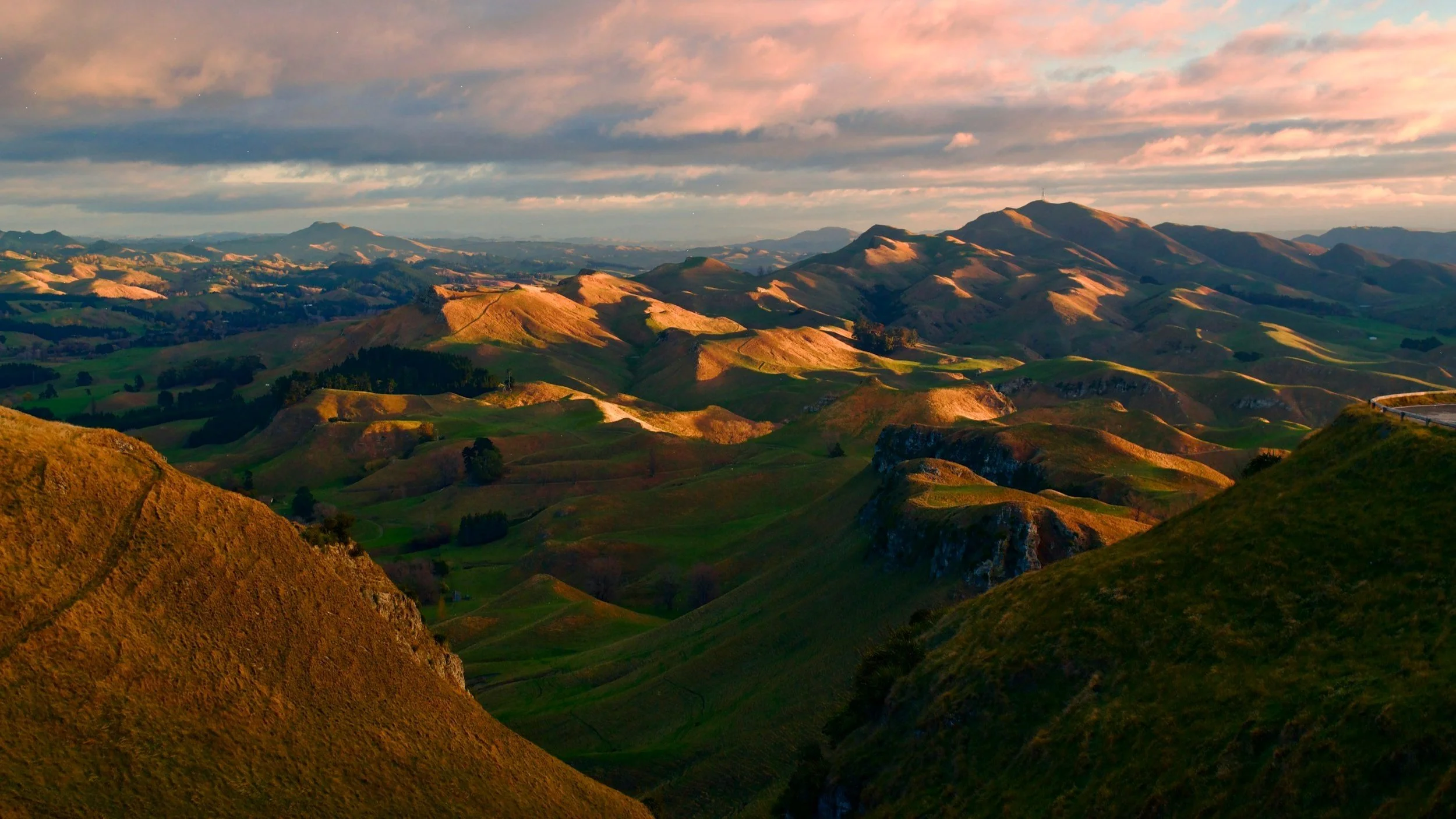Rolling hills landscape with green grass and shadows during sunset, cloudy sky above.