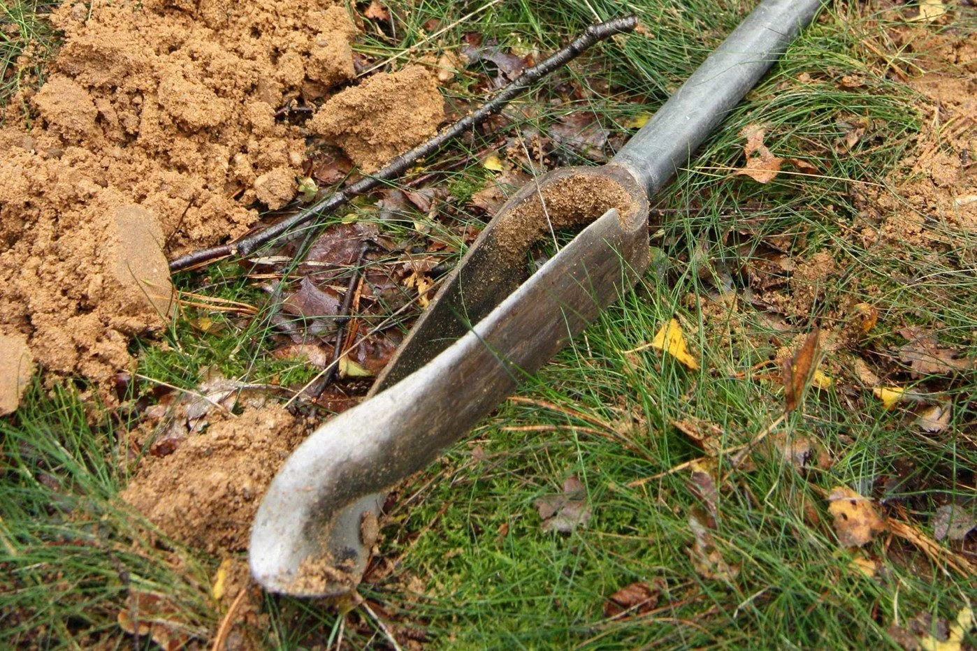 Hand auger with soil, grass, and fallen leaves
