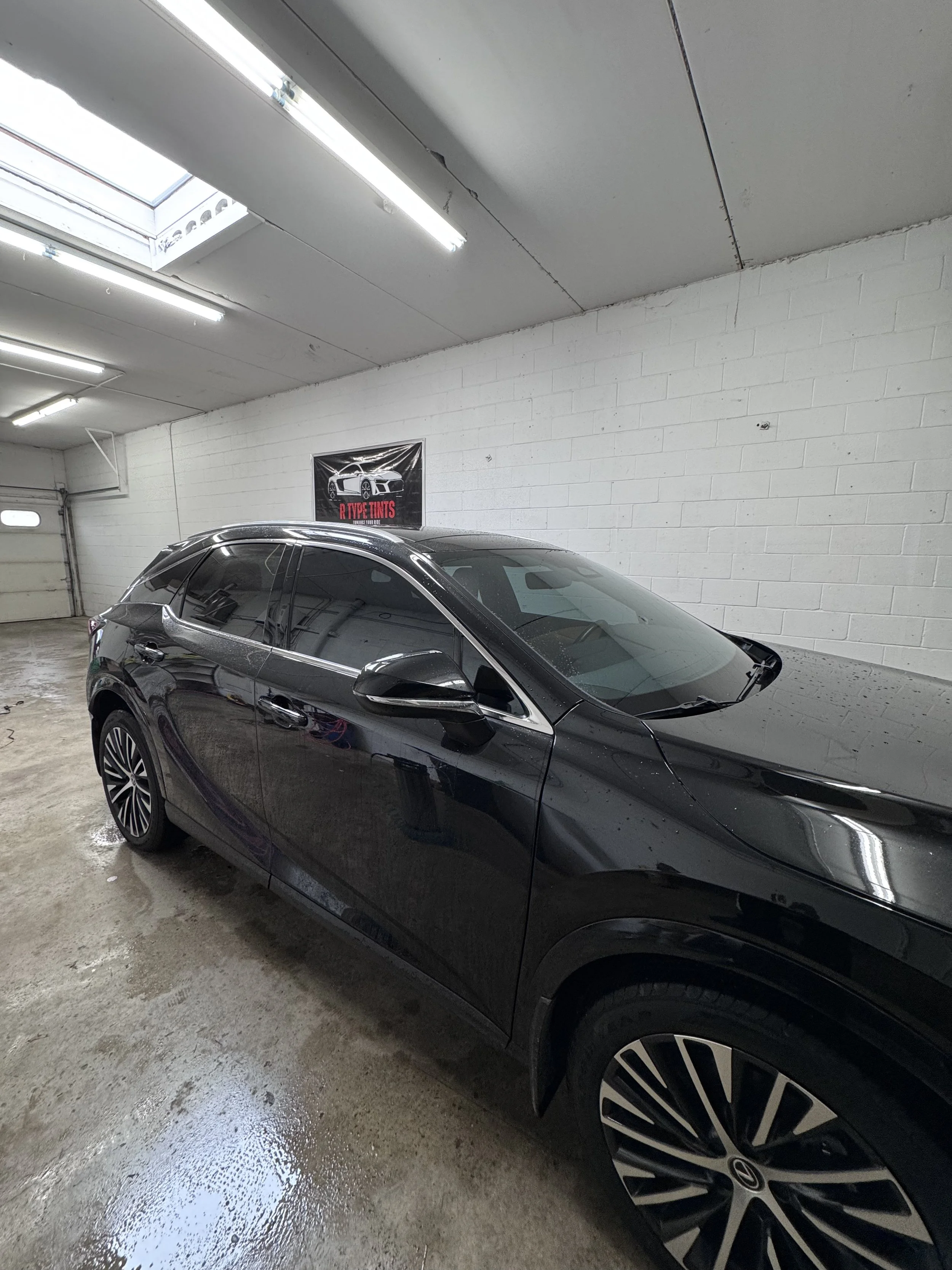 A large aluminum boat on a trailer parked on a paved surface under a cloudy sky, with trees and a small building in the background.