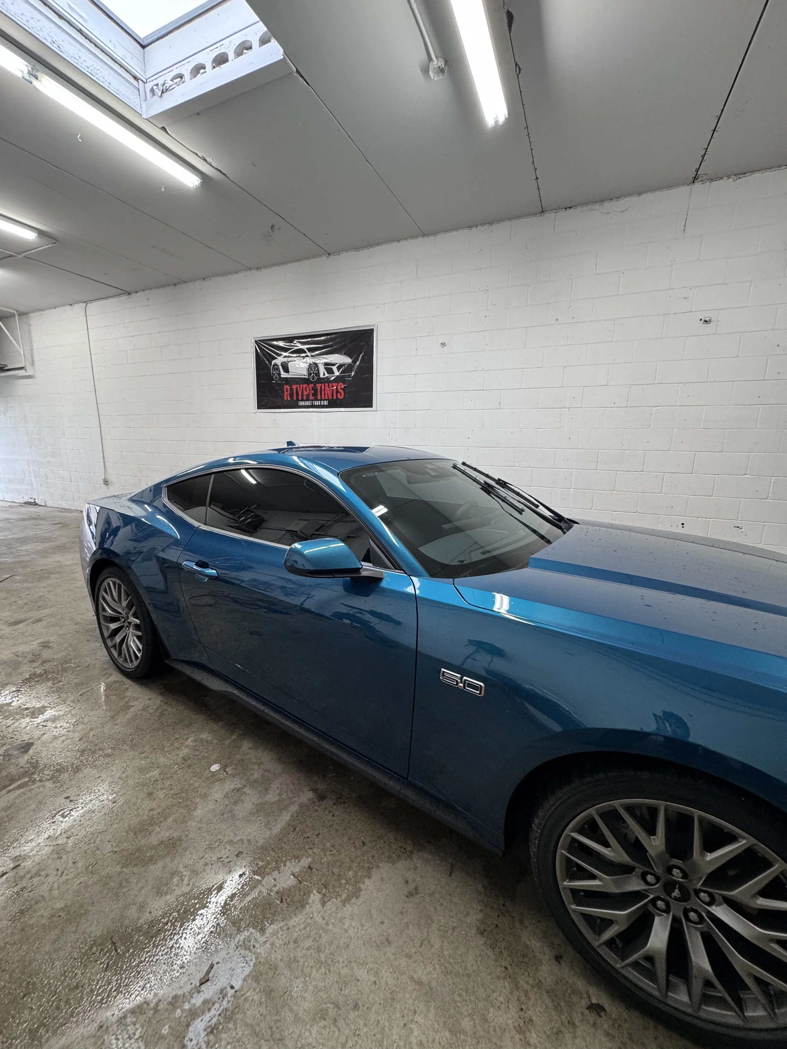 A white modern SUV parked in a parking lot with other cars, a brick building, and cloudy sky.