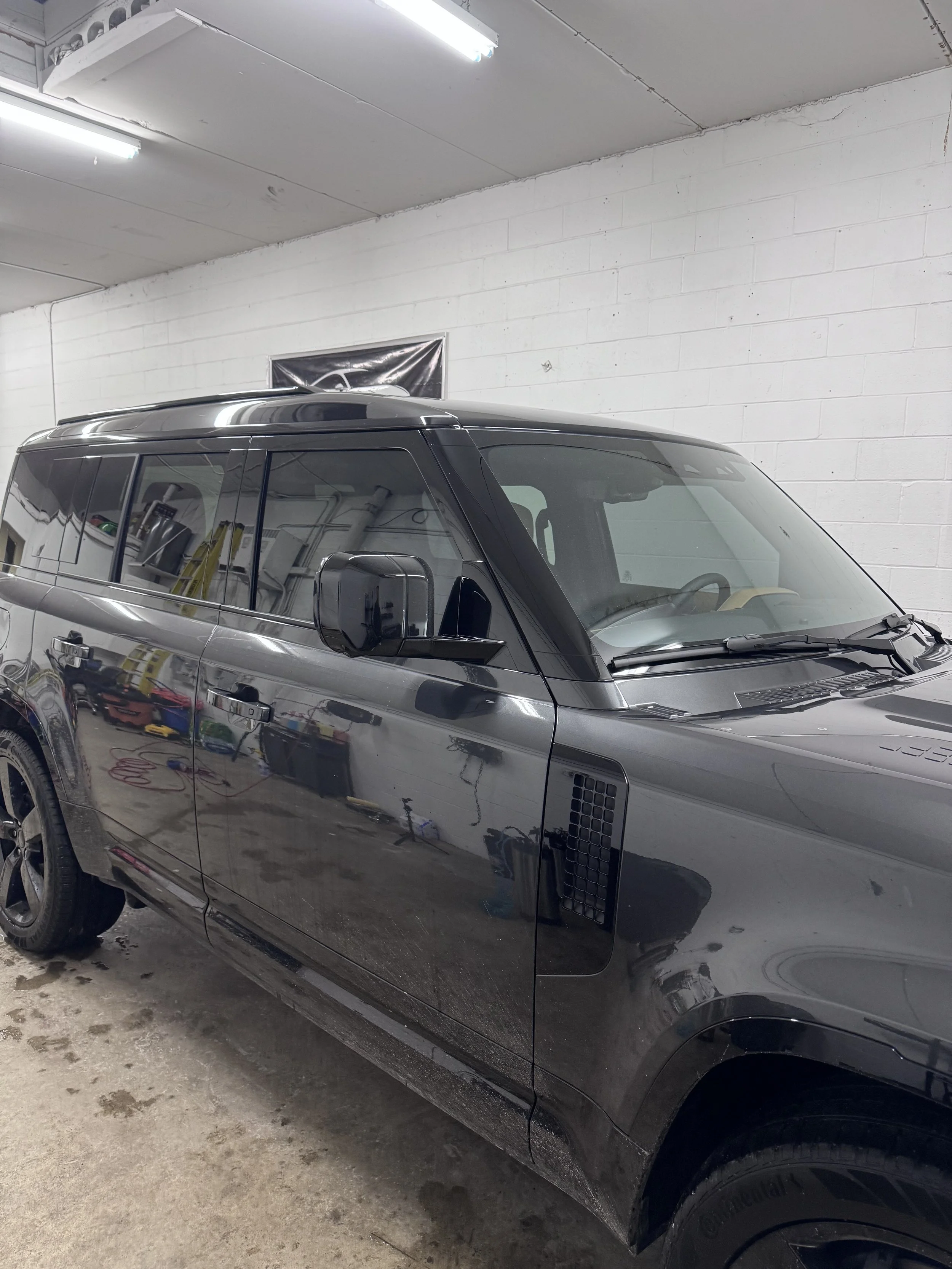 A red Mazda SUV parked on a wet asphalt lot with other cars, a brick building, and a gray overcast sky in the background.