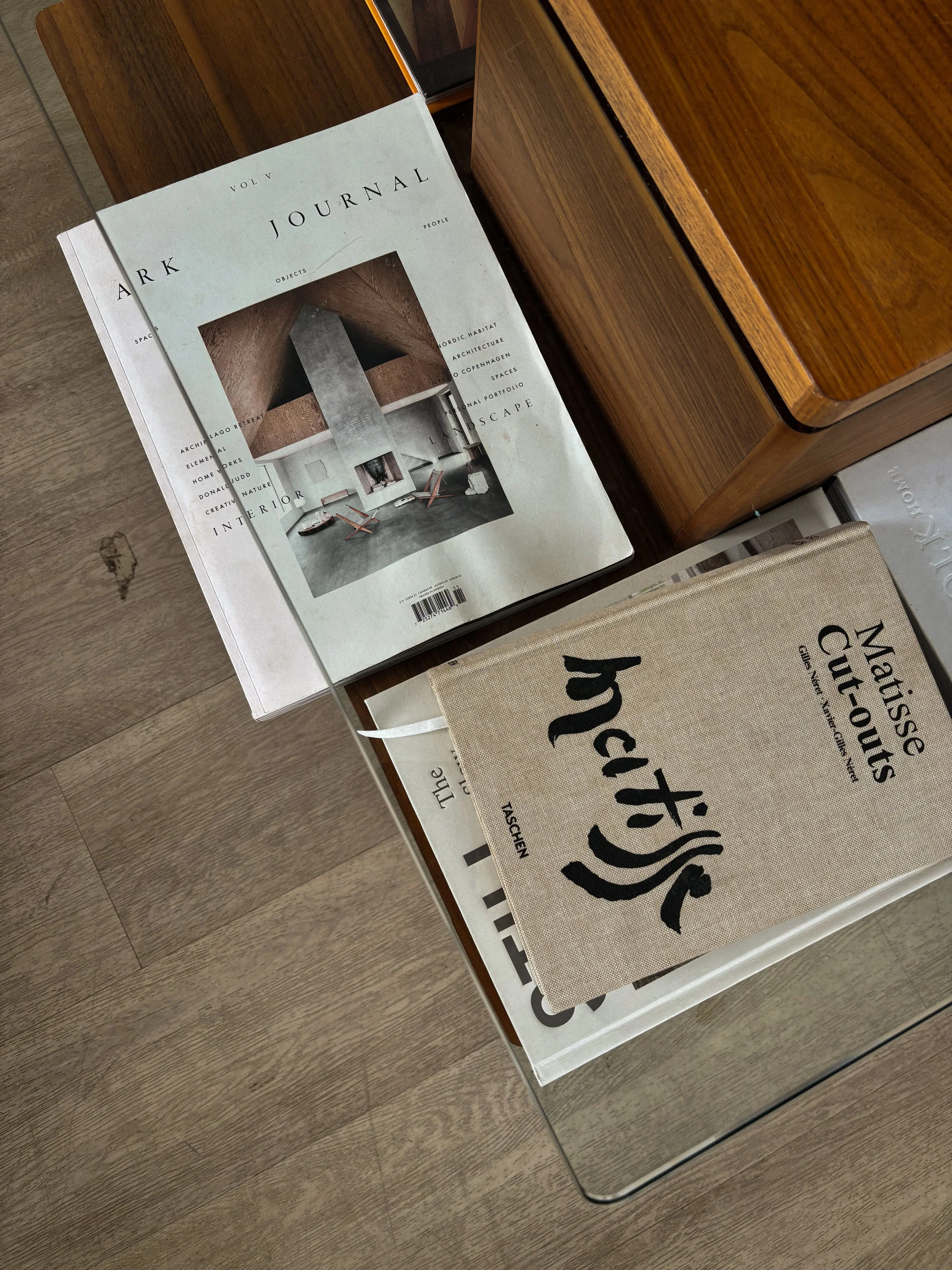 Stack of arts and design magazines and books on a wooden table, including "Ark Journal" and "Matisse Cut-outs."