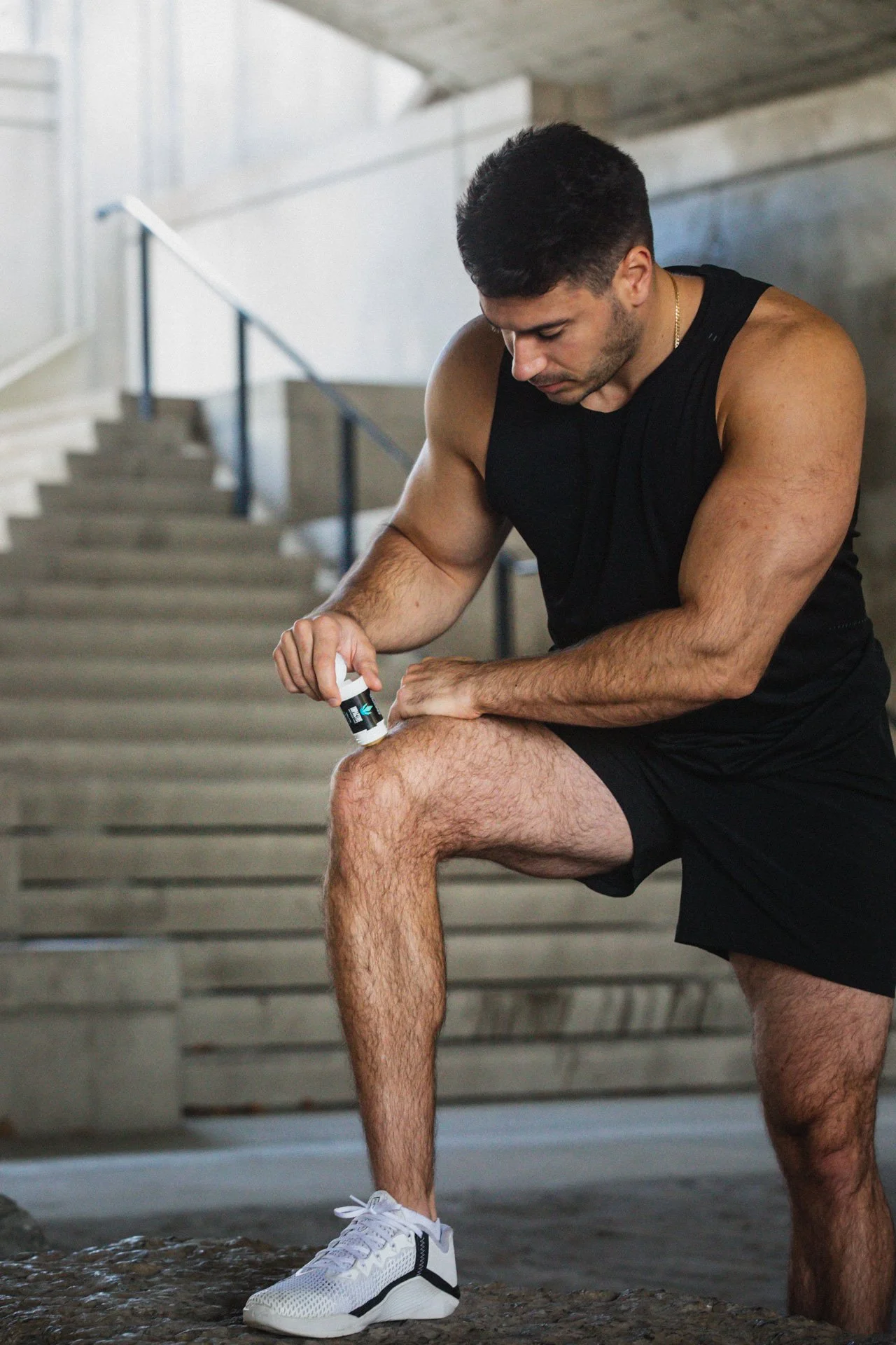 Man in black workout attire applying a product to his knee outdoors.