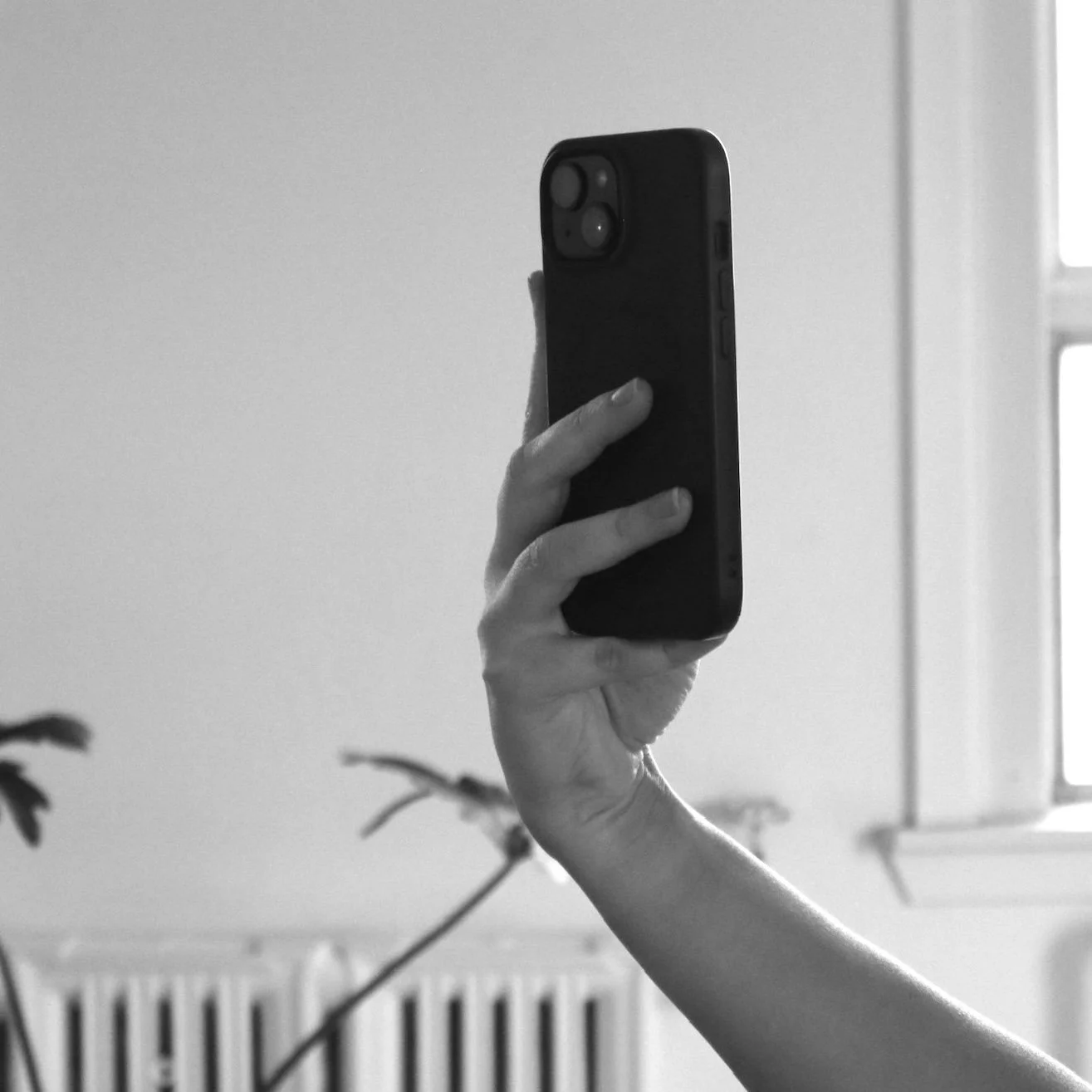 Person holding a smartphone in their hand, taking a selfie in a room.