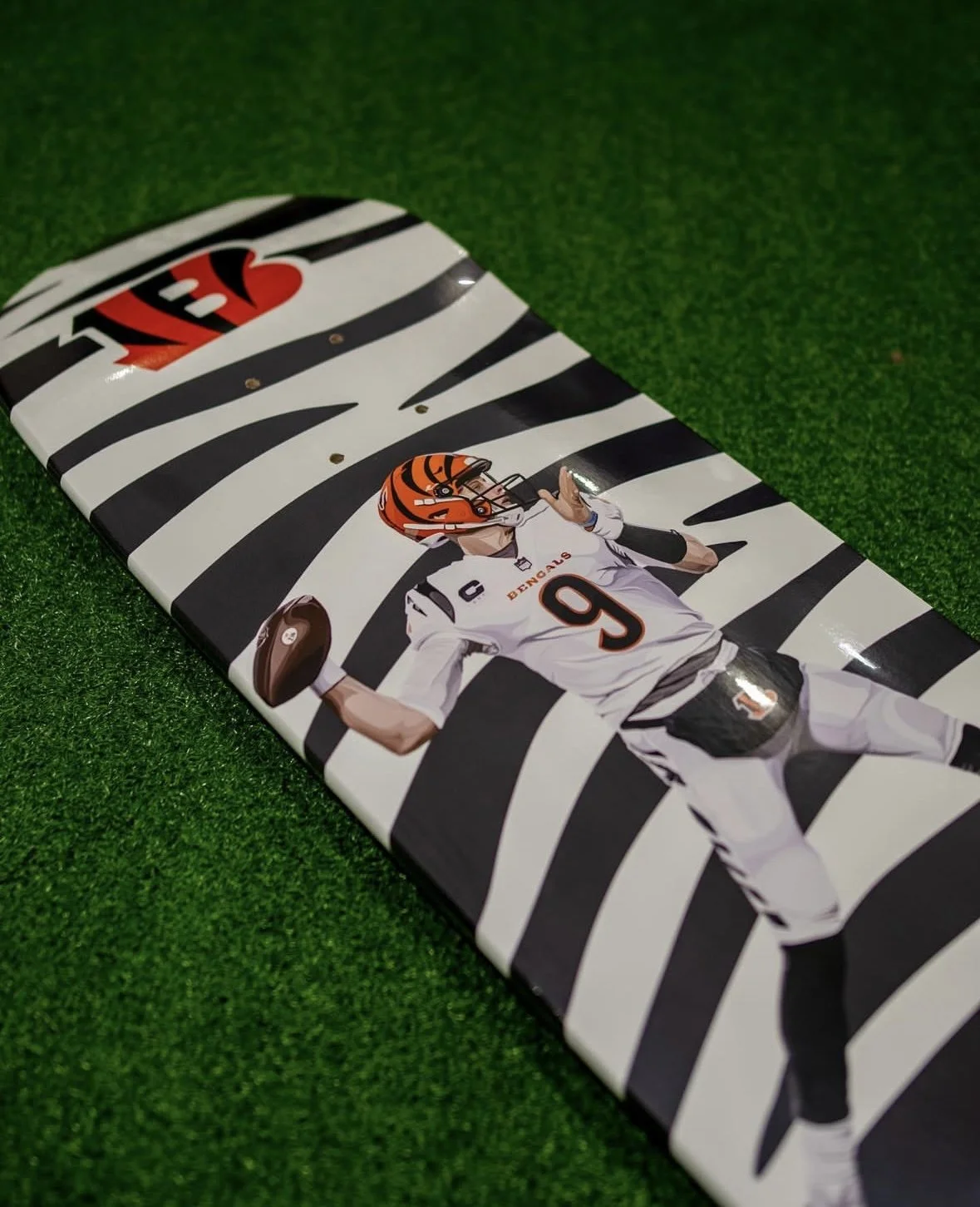 Skateboard deck with football player illustration on zebra stripe background, green grass surface.