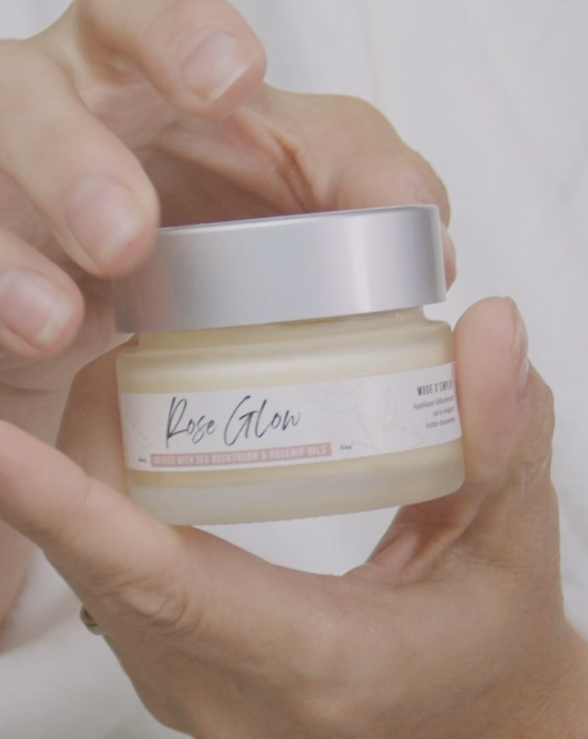 A person holding a jar of "Rose Glow" cream with a silver lid.