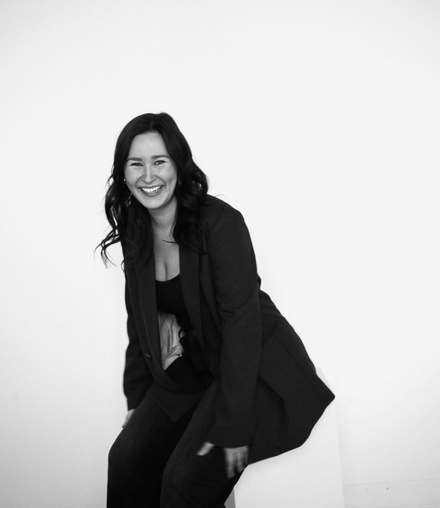Woman smiling in a black and white portrait, wearing a blazer and sitting.