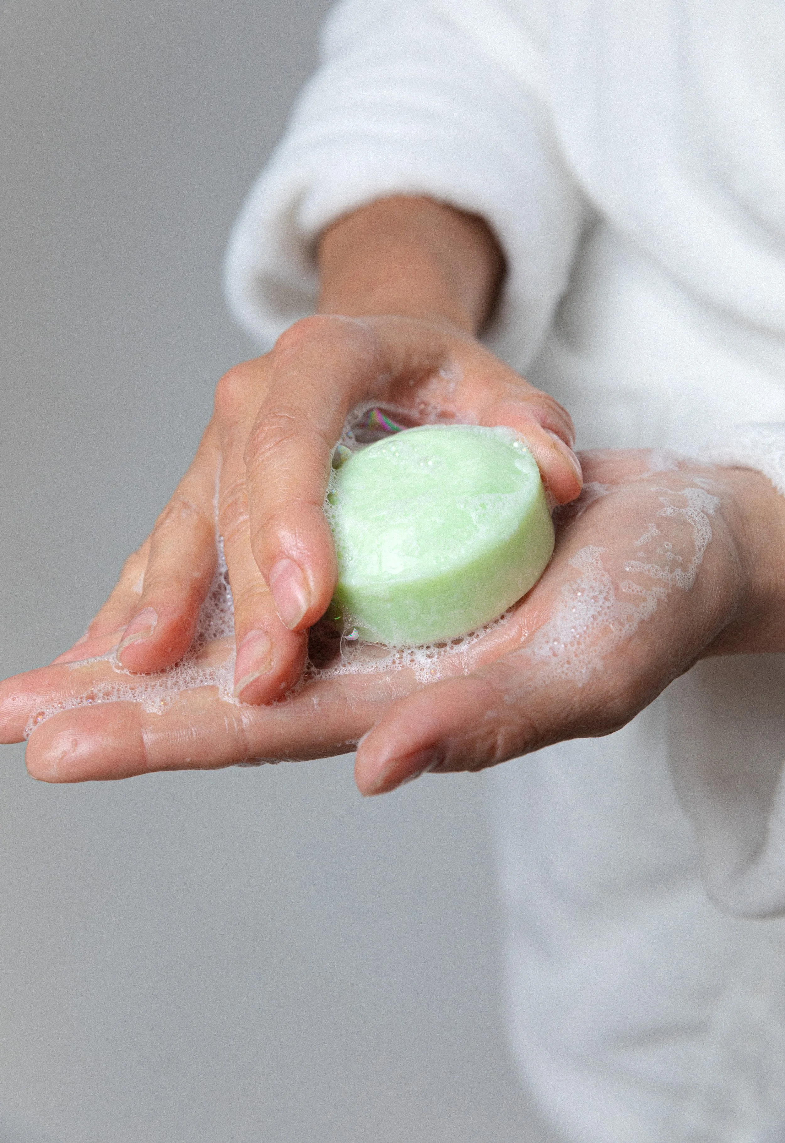 Hands washing with a green soap bar, creating suds.