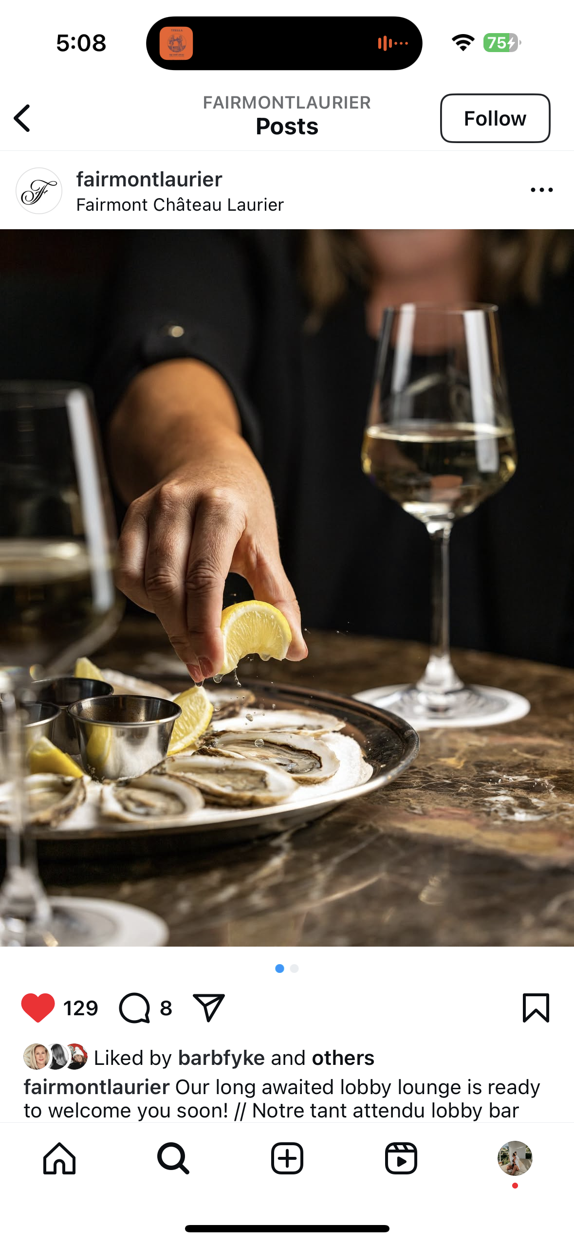Hand squeezing lemon over oysters on a plate with sauce cups, glass of white wine in background.