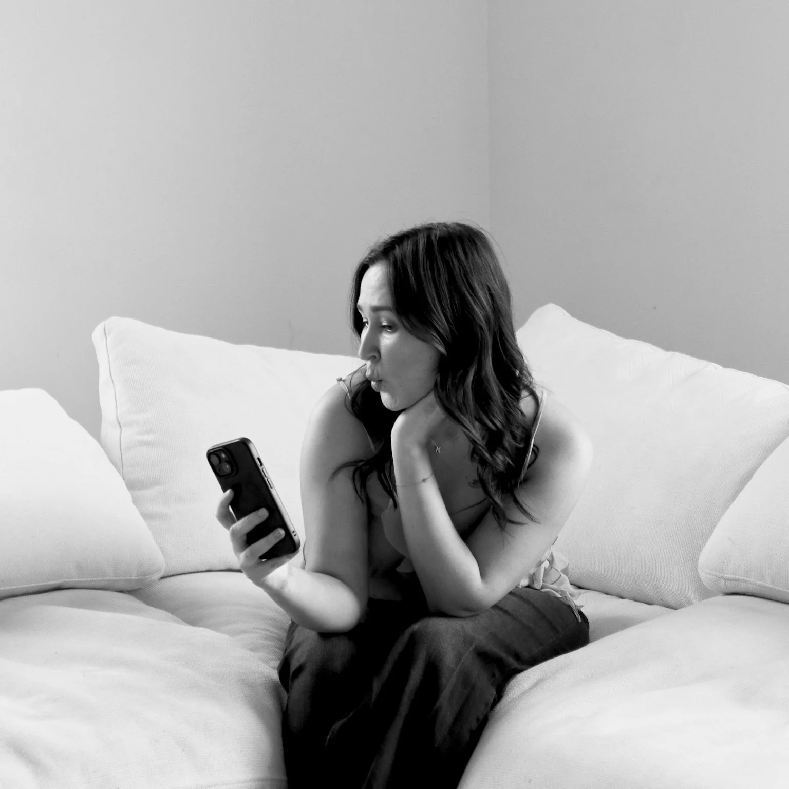 Black and white photo of a woman sitting on a couch, looking at her phone with a surprised expression.