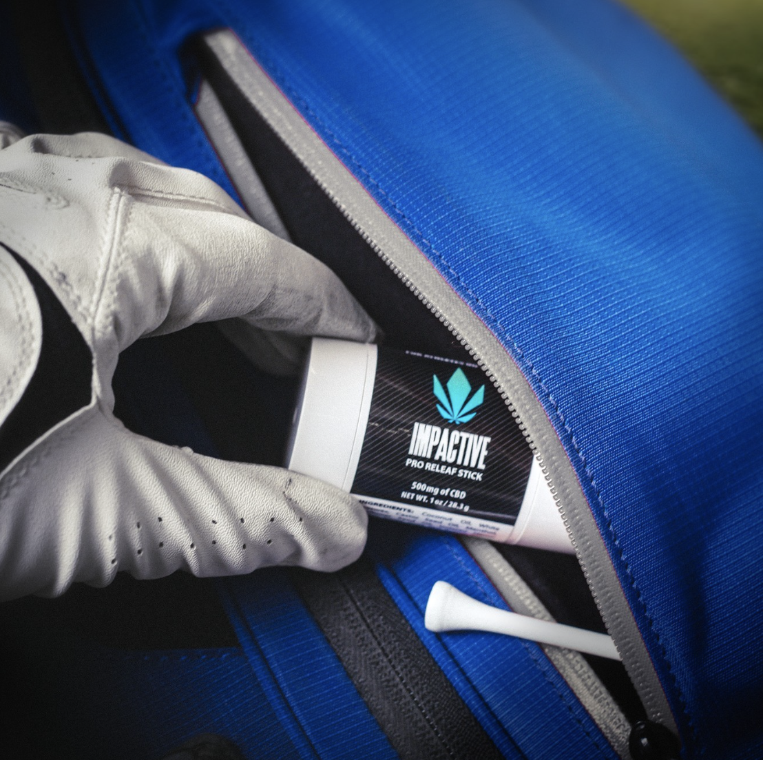 A gloved hand holding an "Impactive Pro Relief Stick" from an open blue bag, with a golf tee visible inside.