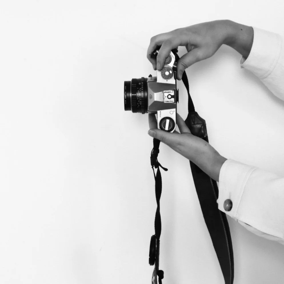 Hands holding a vintage film camera with a strap against a white background.
