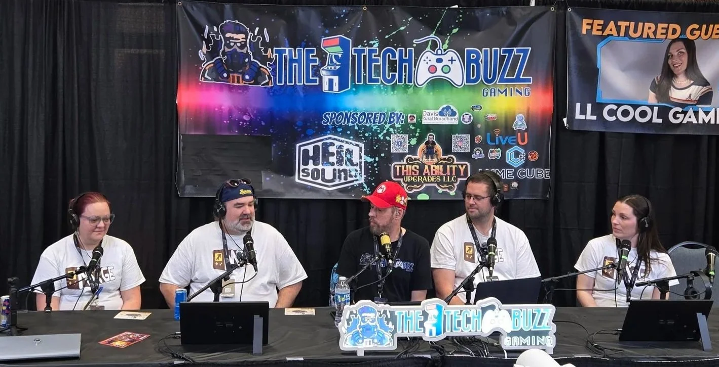 A panel of five people sitting at a table with microphones during a gaming event, with banners in the background featuring the event name 'The Tech Buzz Gaming' and sponsorship logos.