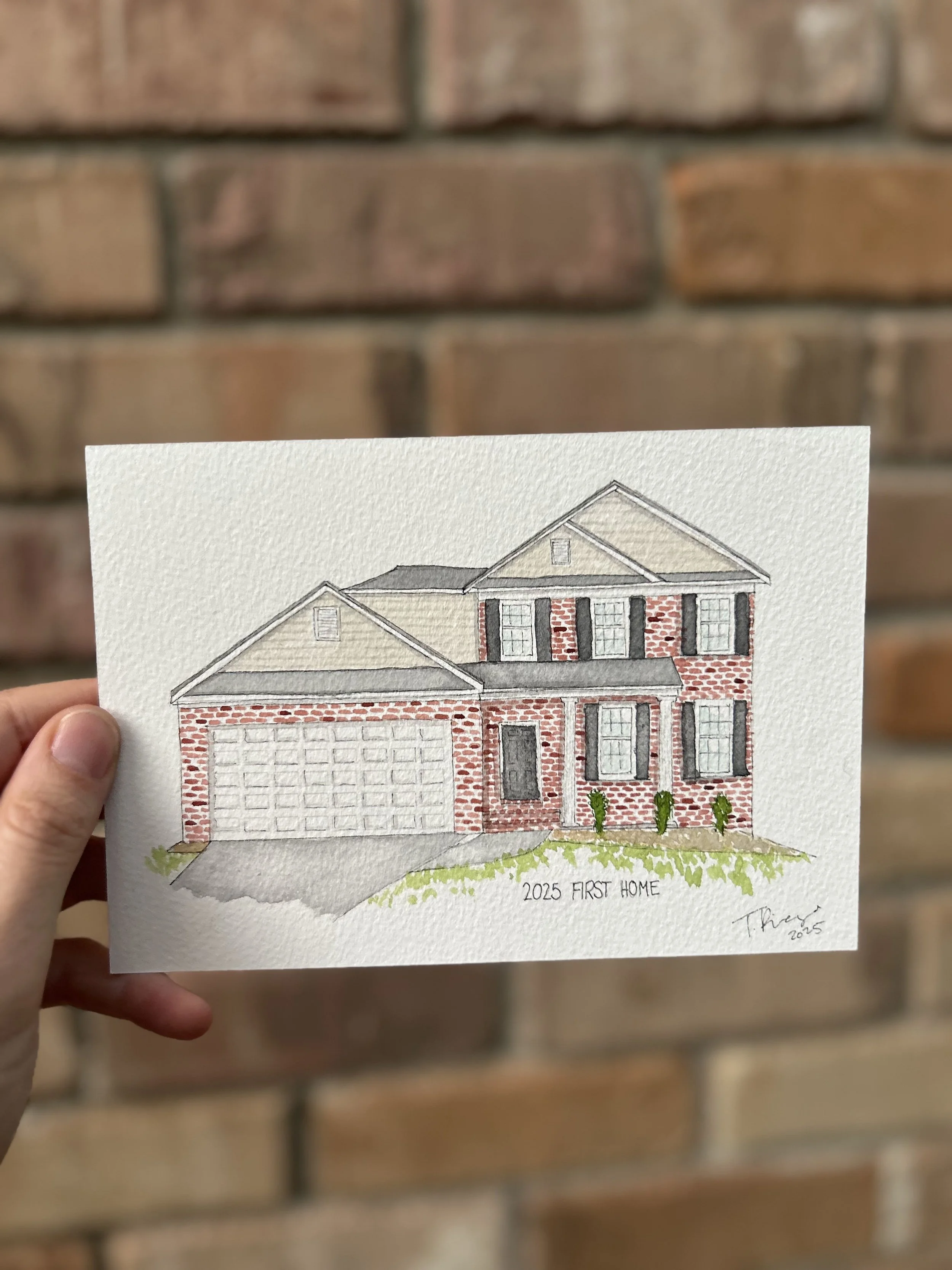Hand holding a colored architectural drawing of a two-story brick house with a garage, front yard, and text that reads '2025 First Home.'