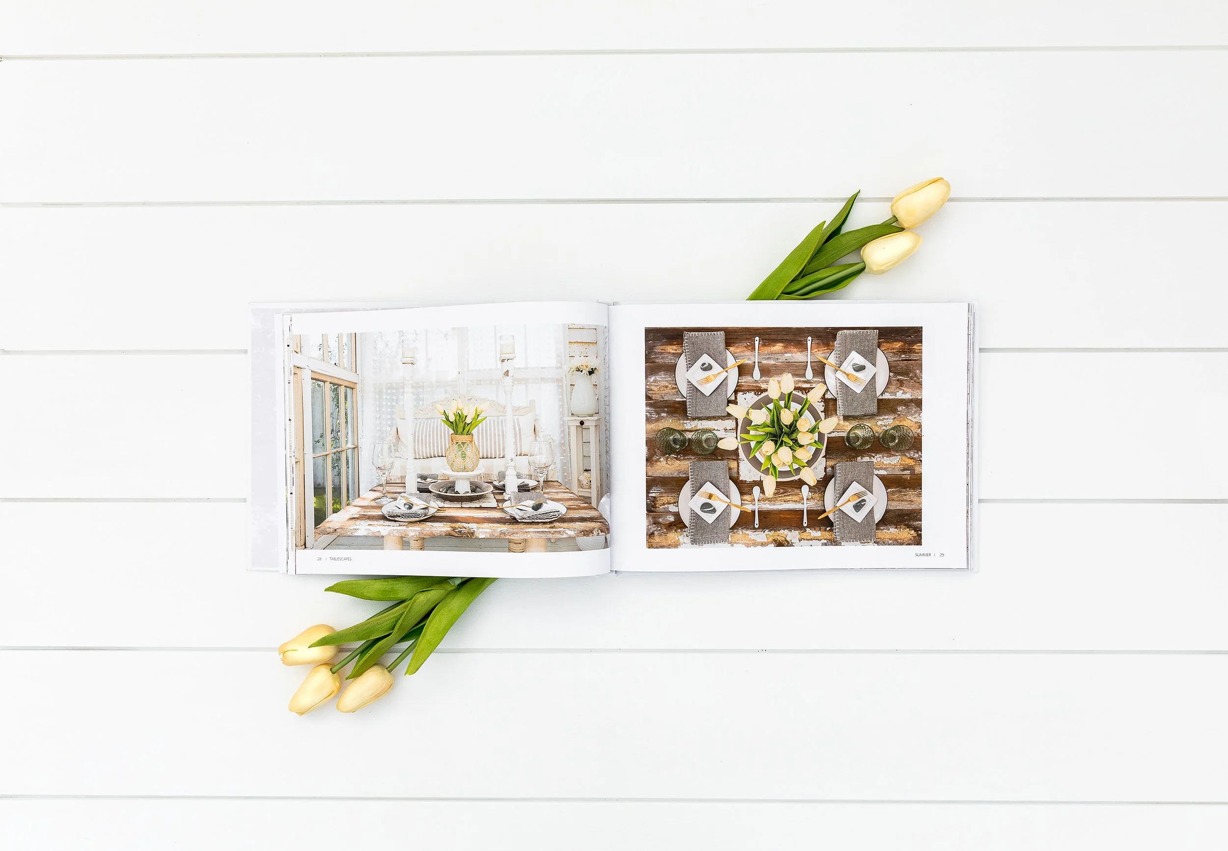 Open book on white table with tulip flowers, displaying images of table settings with elegant place settings and floral arrangements.