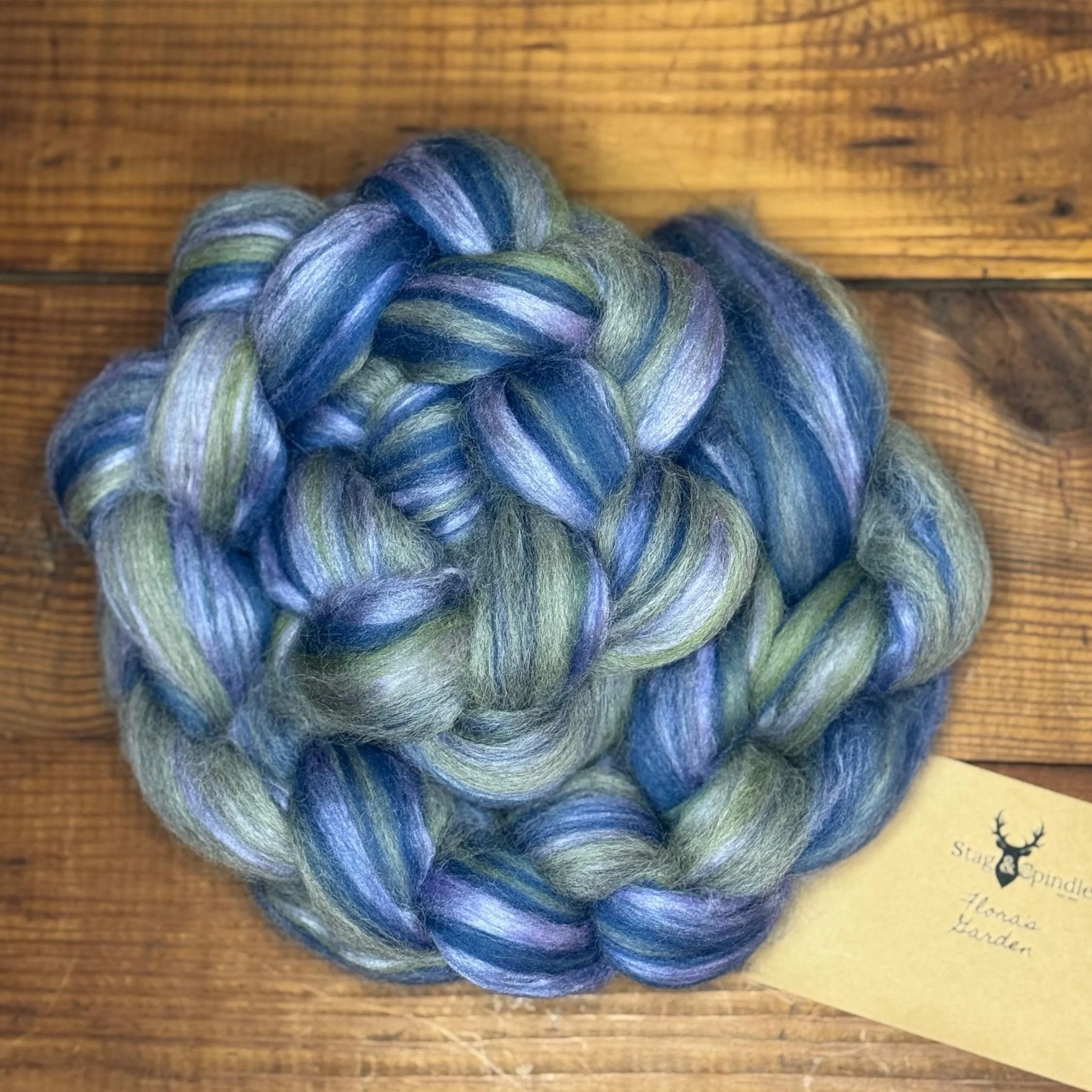 Hand-dyed, multicolored fiber yarn in shades of blue, green, and purple, twisted into a thick braid, on a wooden surface.