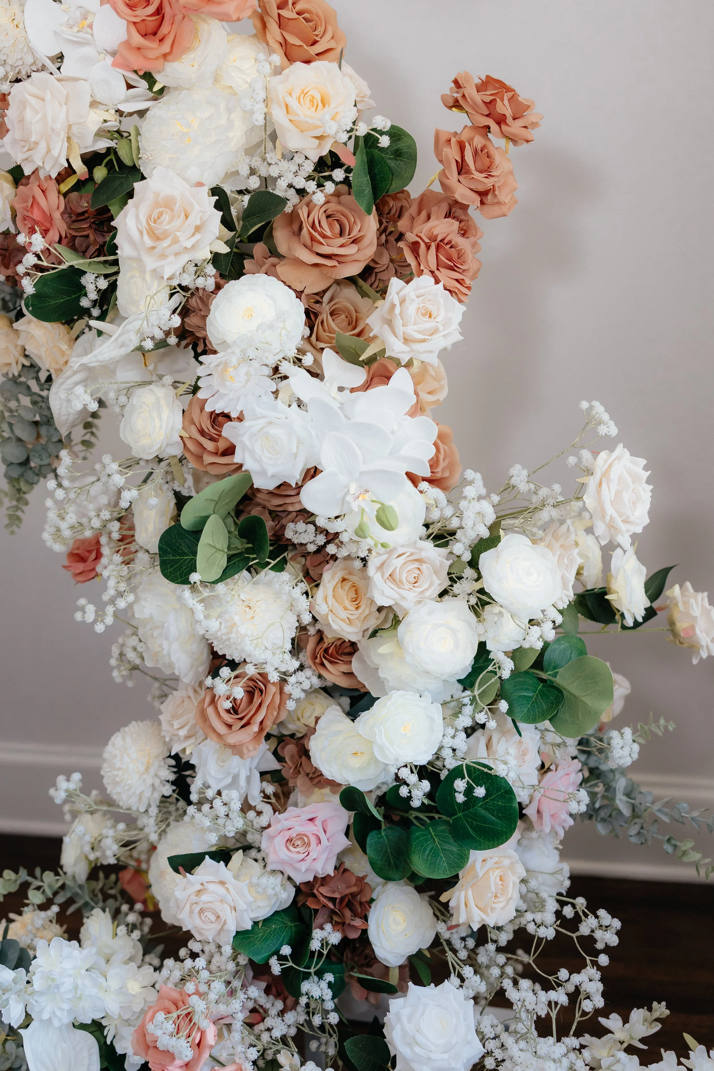 A floral arrangement featuring white, pink, and blush roses mixed with greenery against a neutral background.