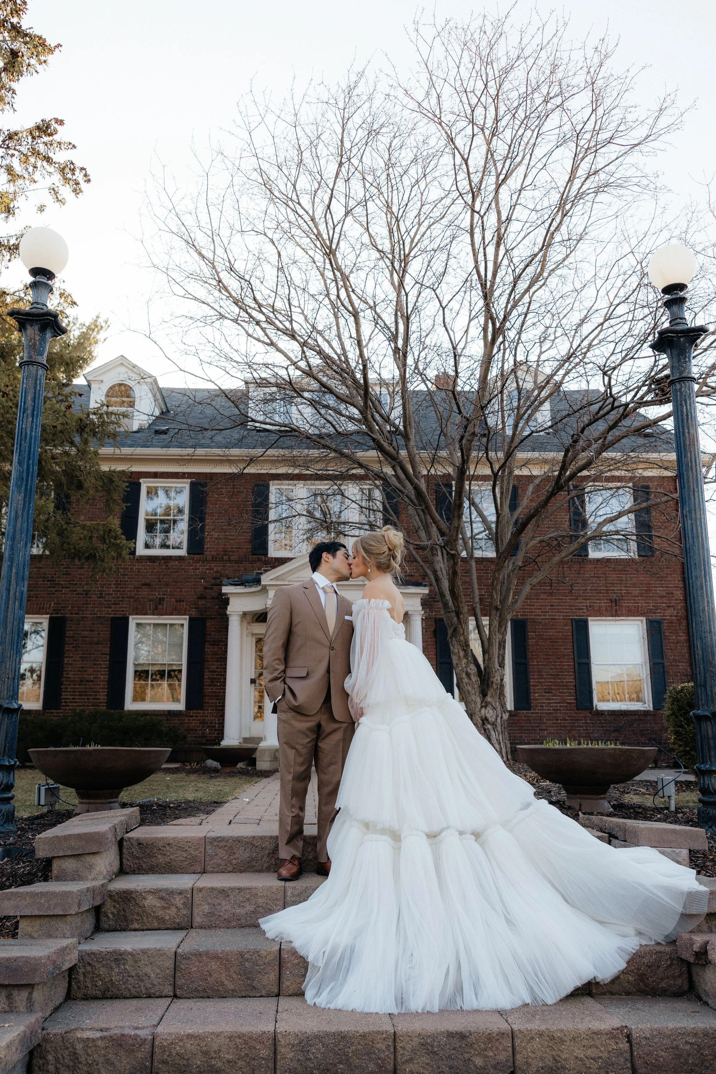 Minnesota Minneapolis Day of Wedding Coordinator. day of coordinator. A couple in wedding attire kissing on stone steps in front of a large, traditional brick building with white columns and dark shutters.