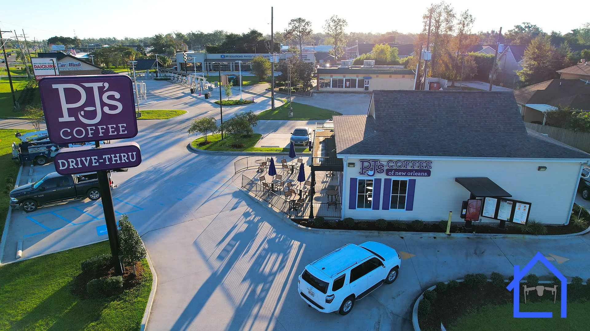 Aerial view of PJ's Coffee in New Orleans with a parking lot, outdoor seating area, and surrounding streets and buildings.