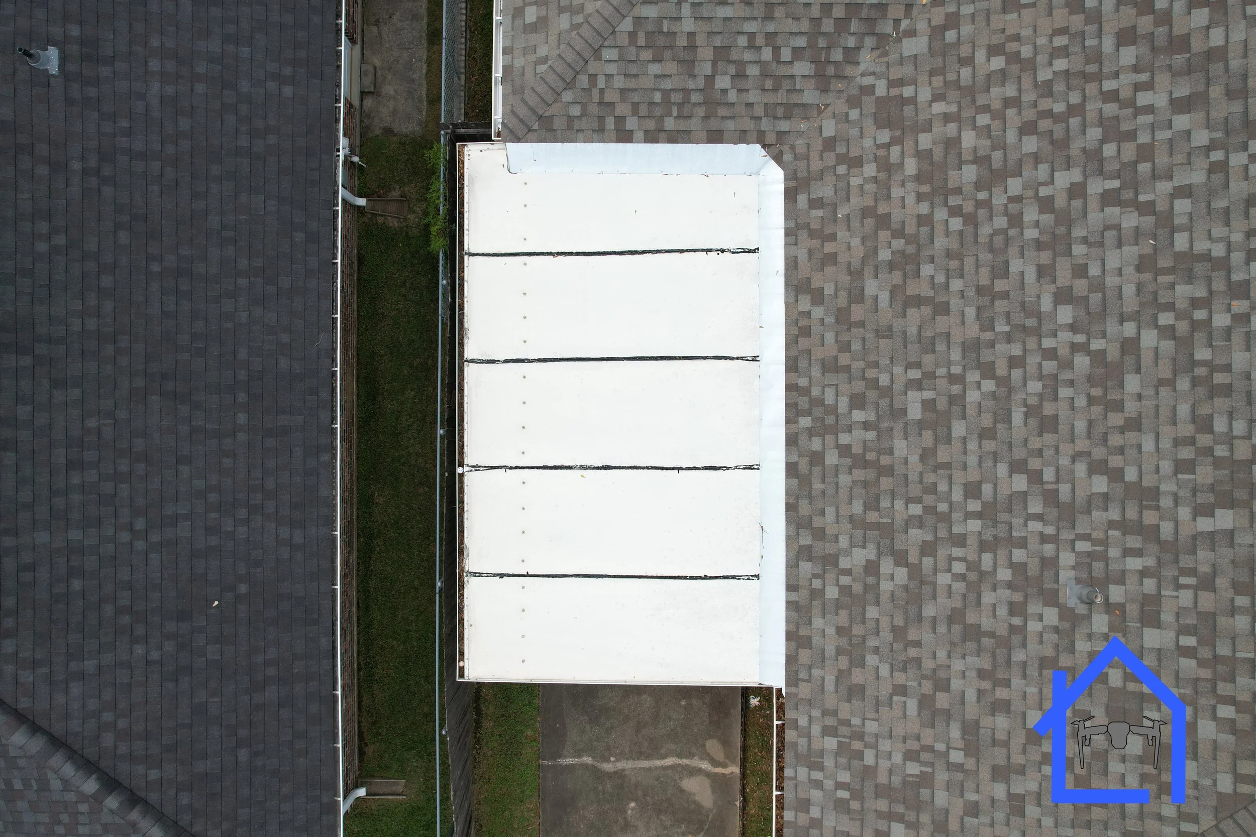 Nadir drone aerial view of a do-it-yourself outdoor roof on a home. The left roof is covered with dark shingles, and the right roof has a white flat section, possibly a garage or patio cover, adjacent to brown shingles.