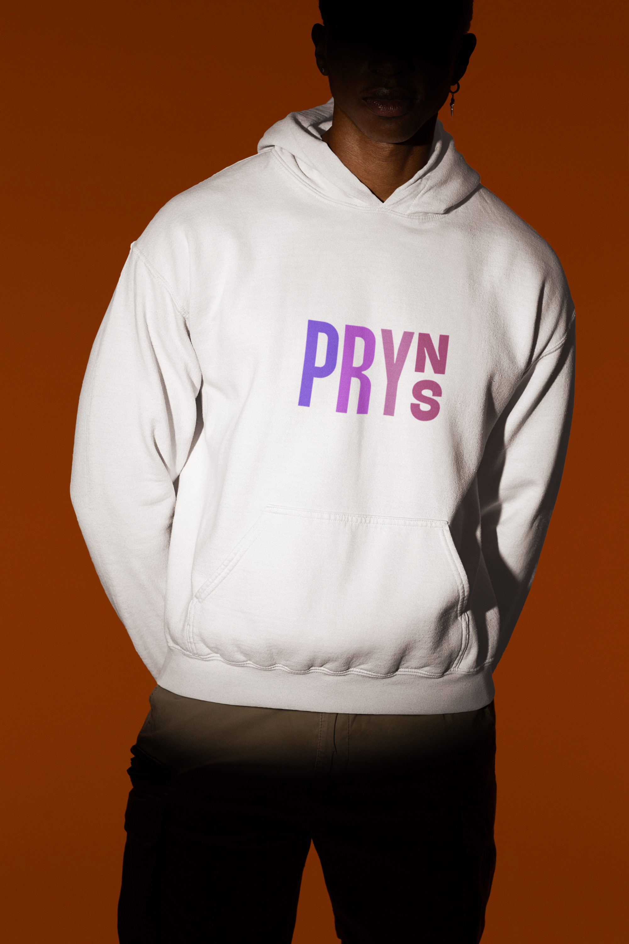 Person wearing a white hoodie with the purple and pink text 'PRY' and 'S' on the front, standing against a dark orange background.