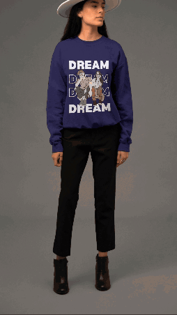 A woman wearing a navy blue sweatshirt with a unicorn graphic and the words 'DREAM' repeated three times, black pants, and black ankle boots, standing against a gray background.