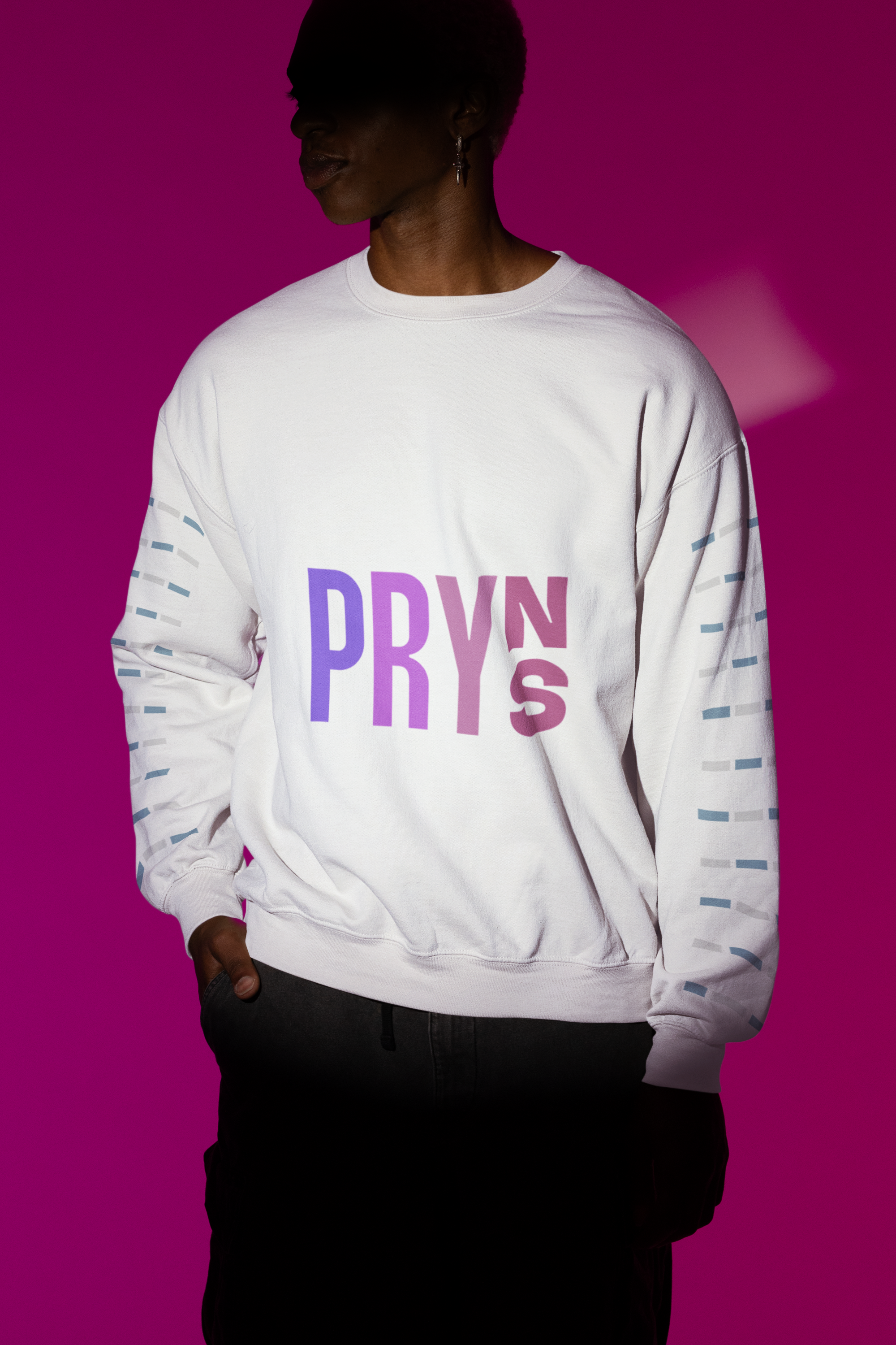 Person wearing a white sweatshirt with the word 'PRYNS' printed in purple and pink letters against a pink background.