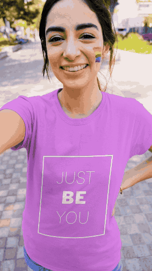 Smiling young woman with face paint, wearing a purple T-shirt that says 'Just Be You', taking a selfie outdoors on a sunny day.
