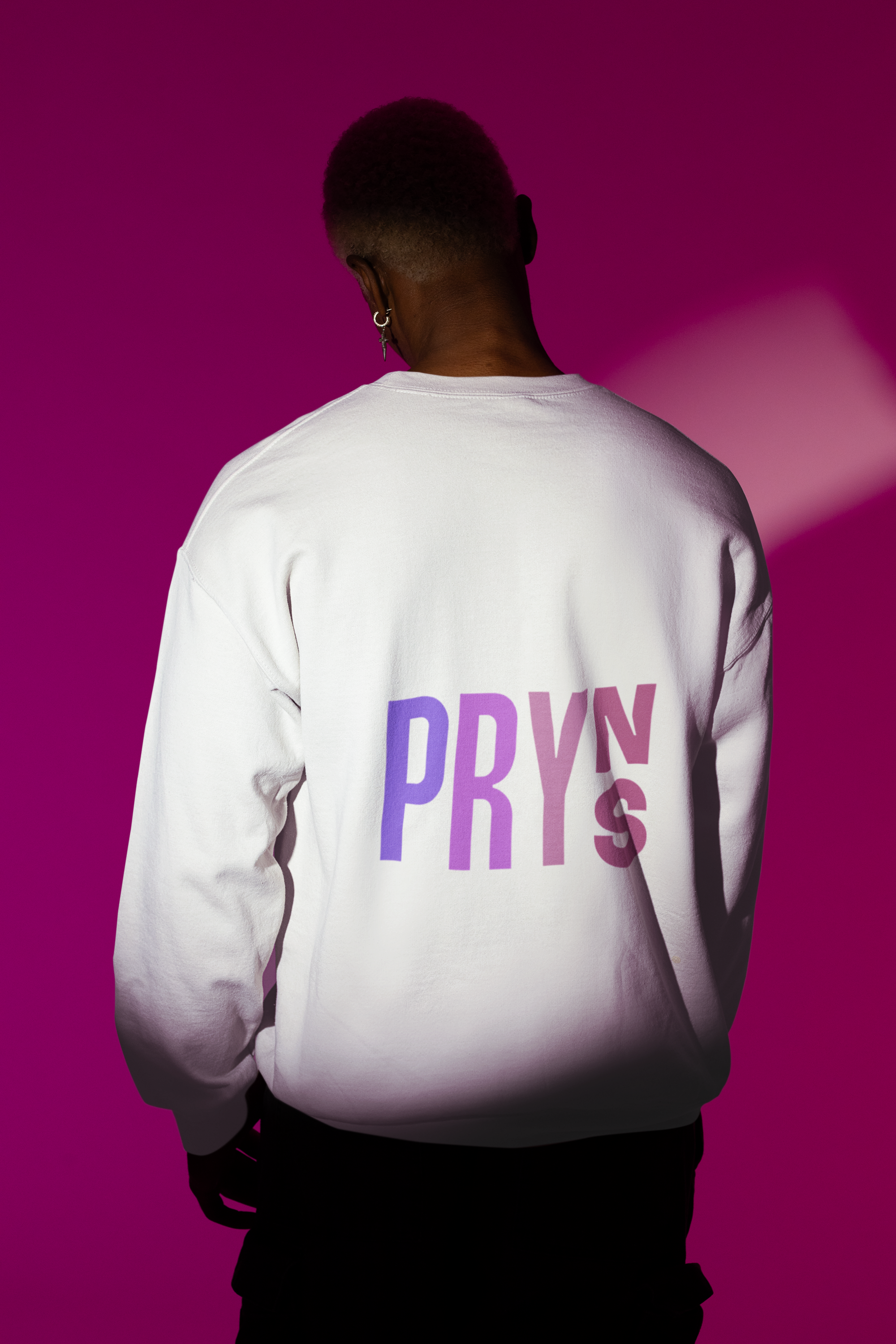 Person wearing a white sweatshirt with purple text "PRYN" on the back, facing away against a pink and purple background.