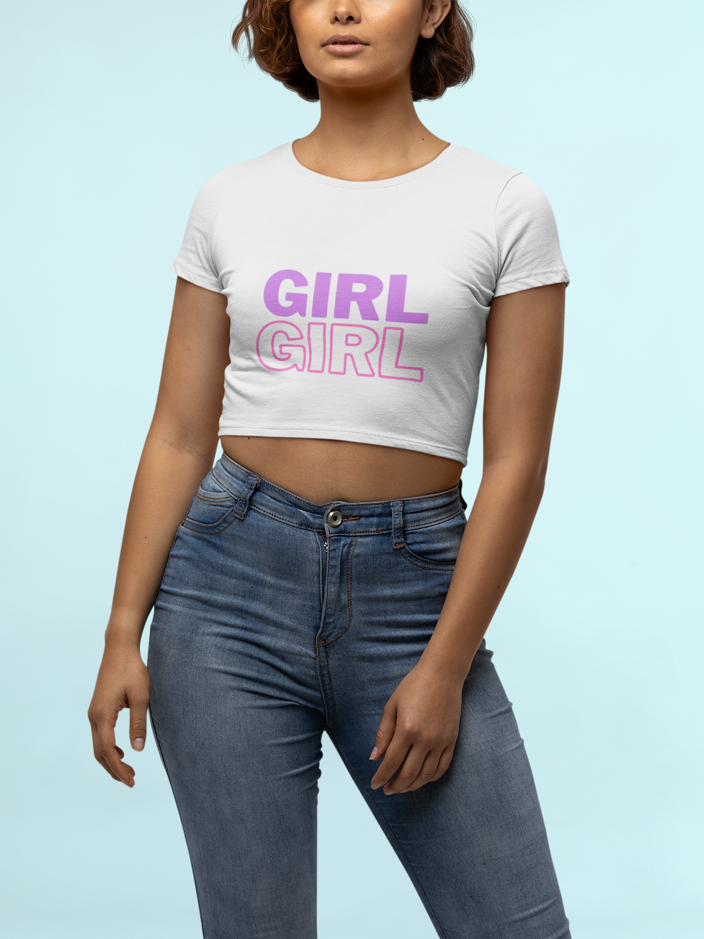 A woman wearing a white crop top with the word 'GIRL' written twice in purple and pink, paired with blue jeans.