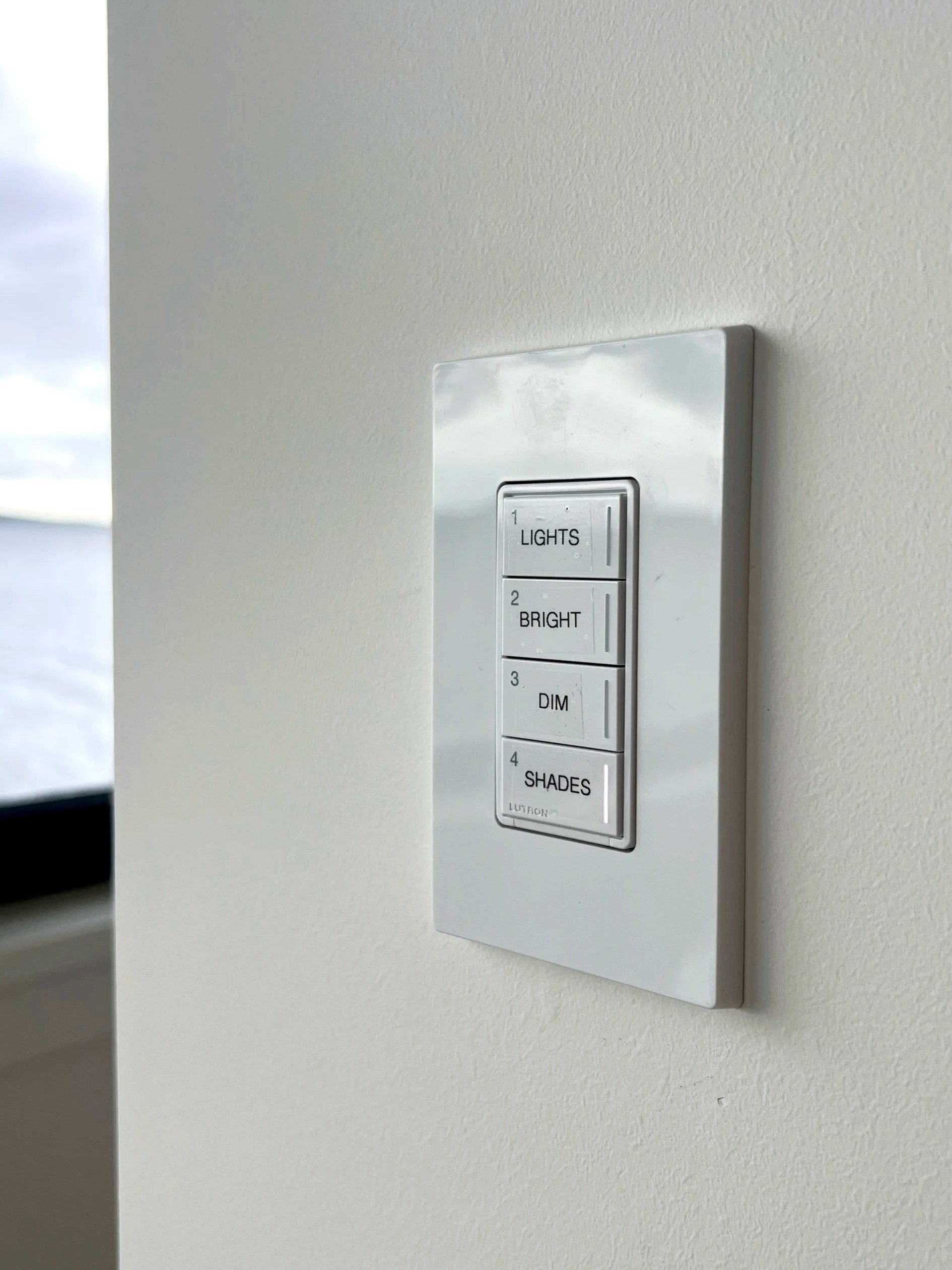 Close-up of modernlutron control panels on a stainless steel wall, with two black stools below, in a minimalistic interior space.