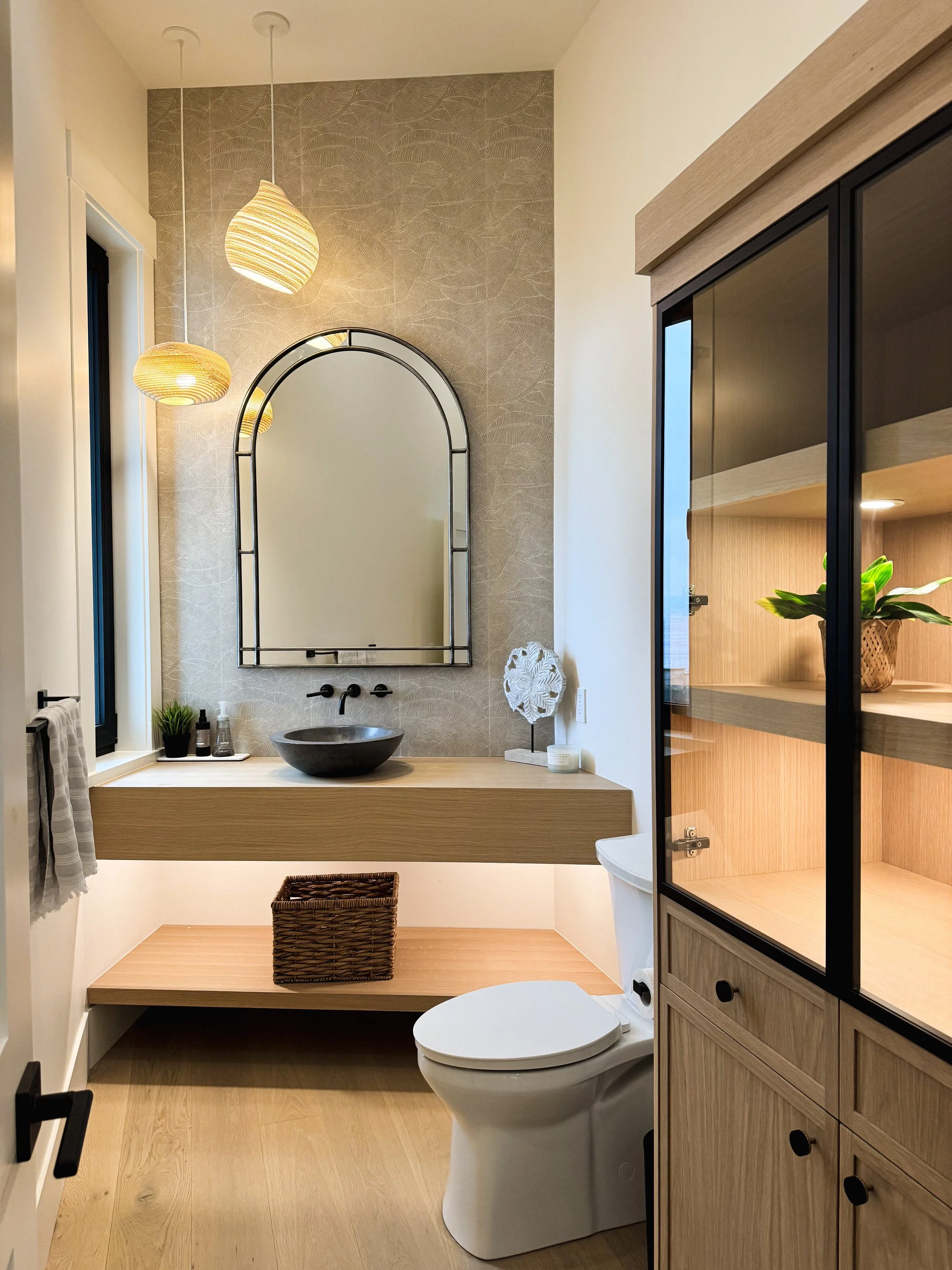 A two-story house with large windows, wood siding, and a sloped roof, illuminated at dusk, with a garden and pathway in the foreground.