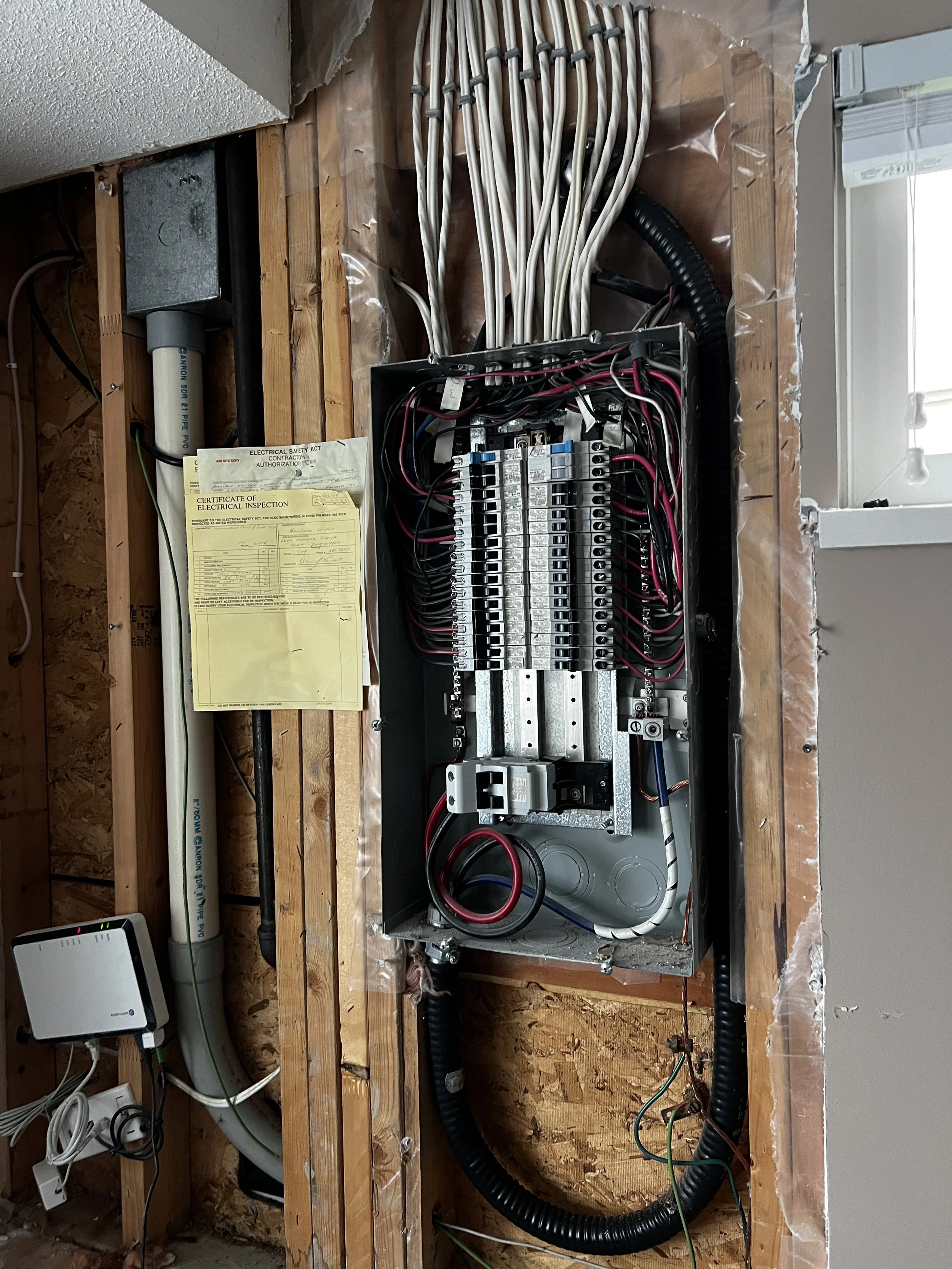 Electricians working on wiring in an unfinished wall with a breaker box, various cables, and electrical components.