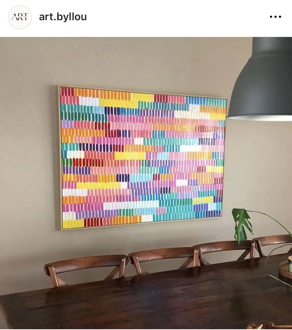 Colorful abstract painting with vertical brushstrokes on a wall above a wooden dining table and chairs.